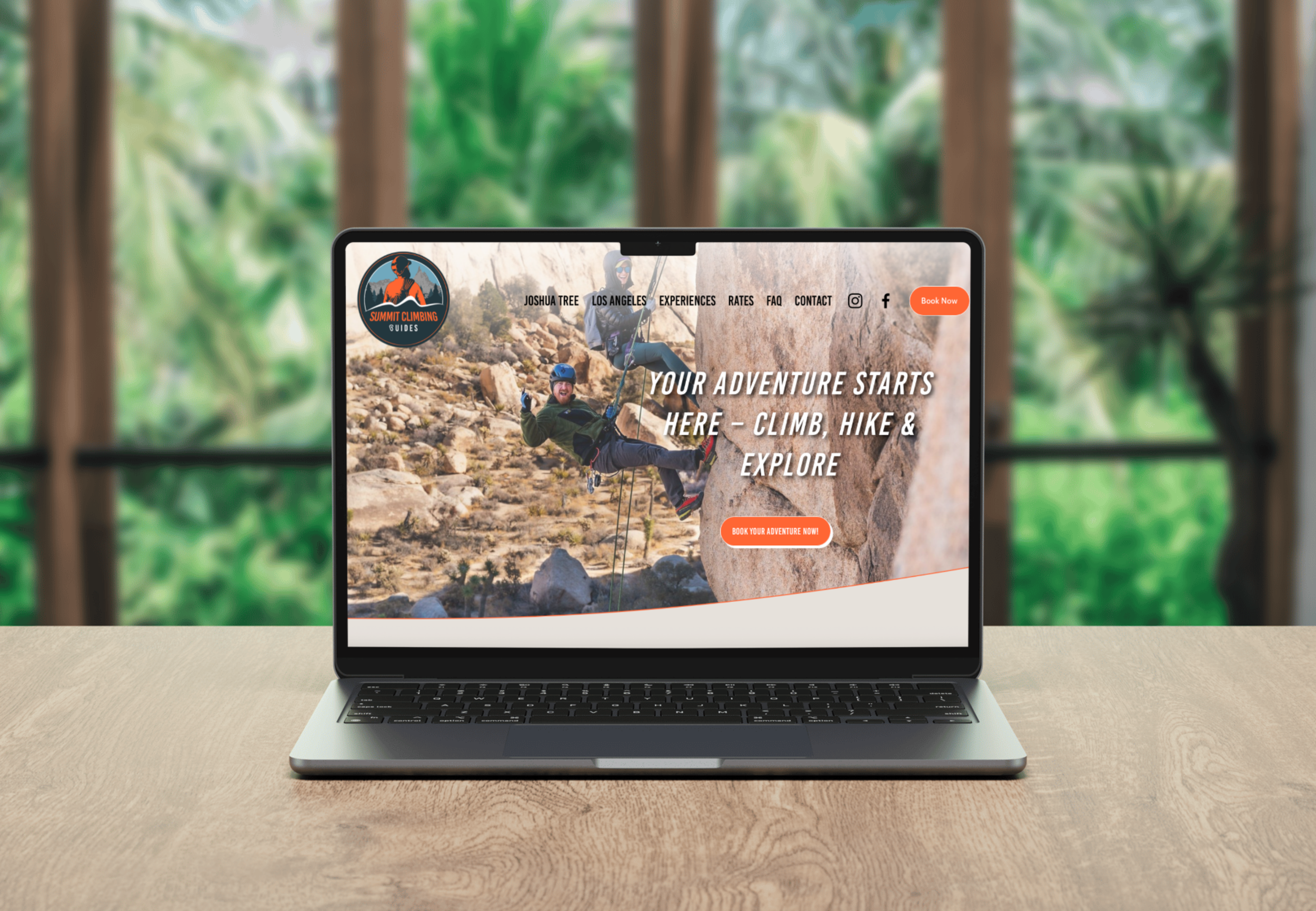 Laptop on a wooden table displaying a climbing adventure website, with a background of blurred greenery outside a window.