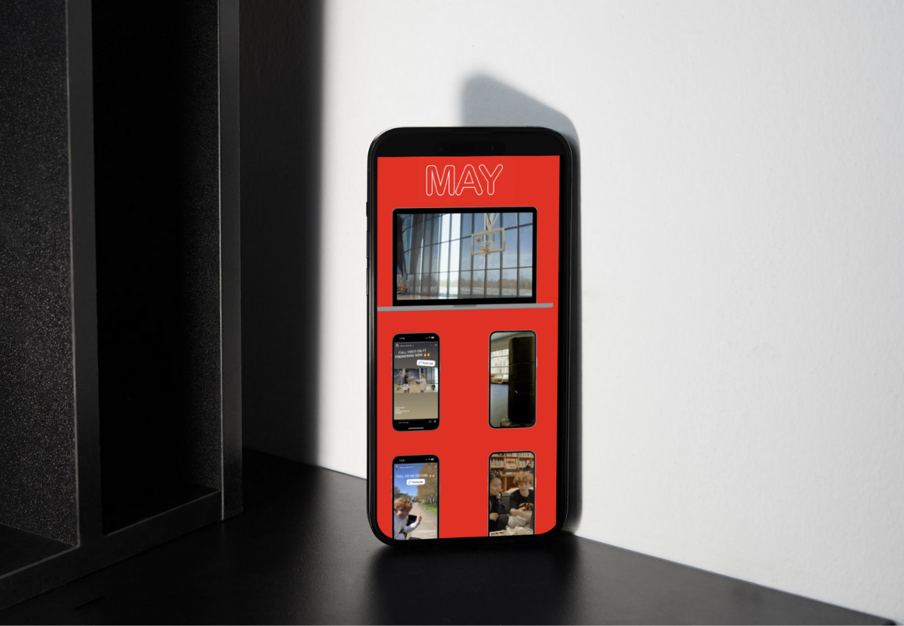 A smartphone with a red background displaying a collage of images, including a basketball hoop, a child with a puppy, and people at outdoor events, placed on a black surface against a white wall.