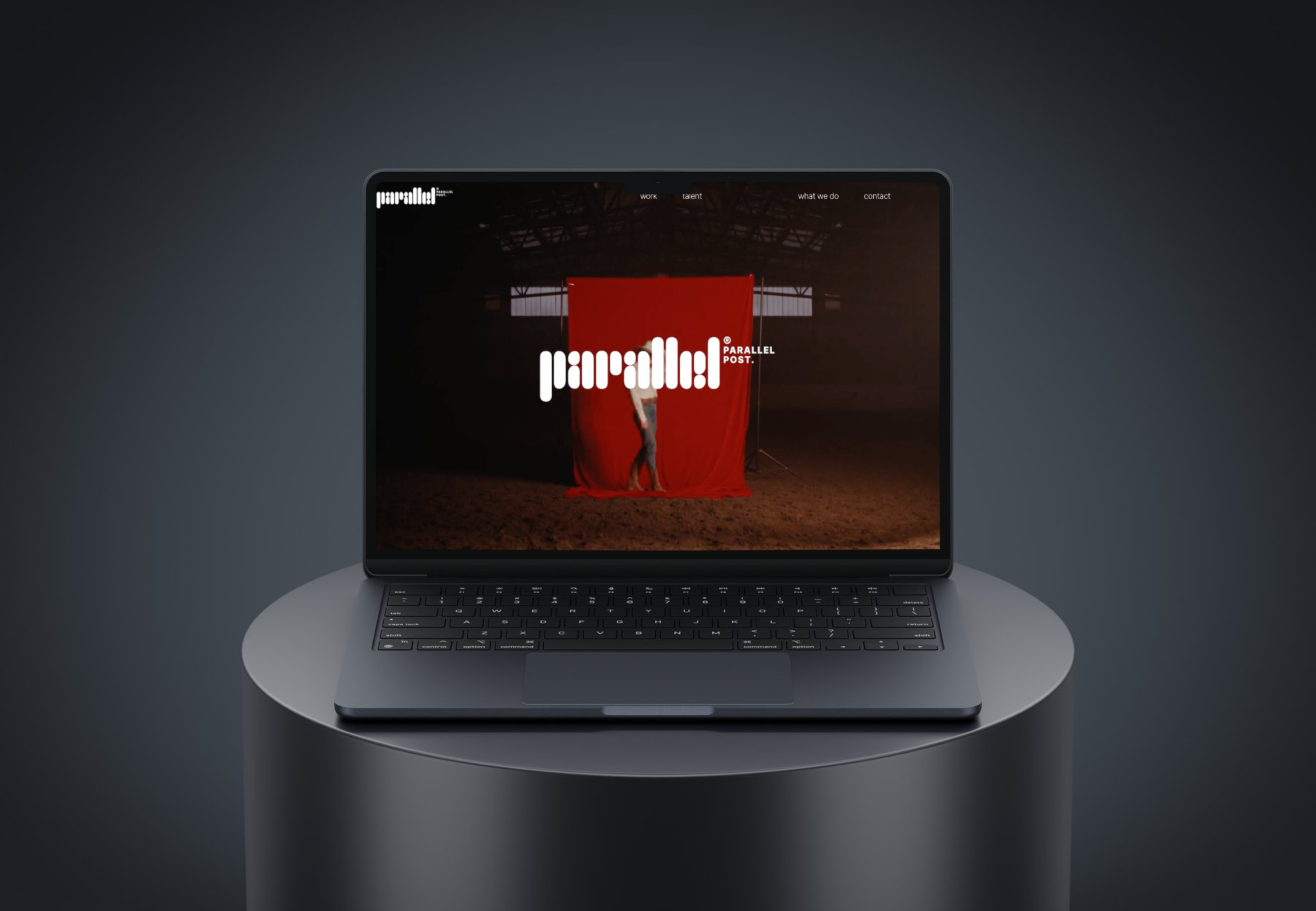 Laptop displaying a website with a dark background, a red curtain, and a person partially visible behind it, with white text overlay reading 'parallel! POST'.