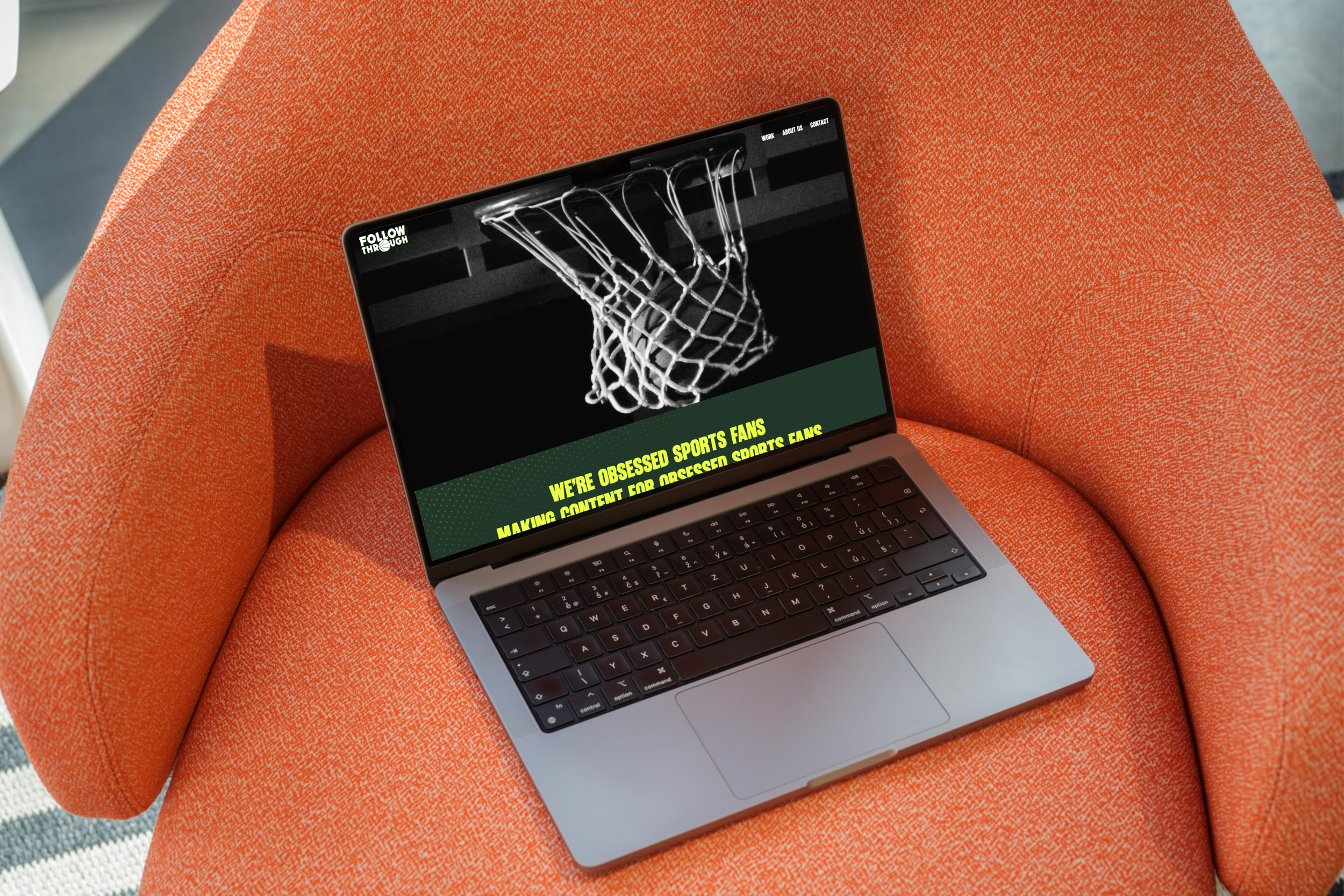 A laptop displaying a website with a basketball hoop and net, resting on an orange textured chair.