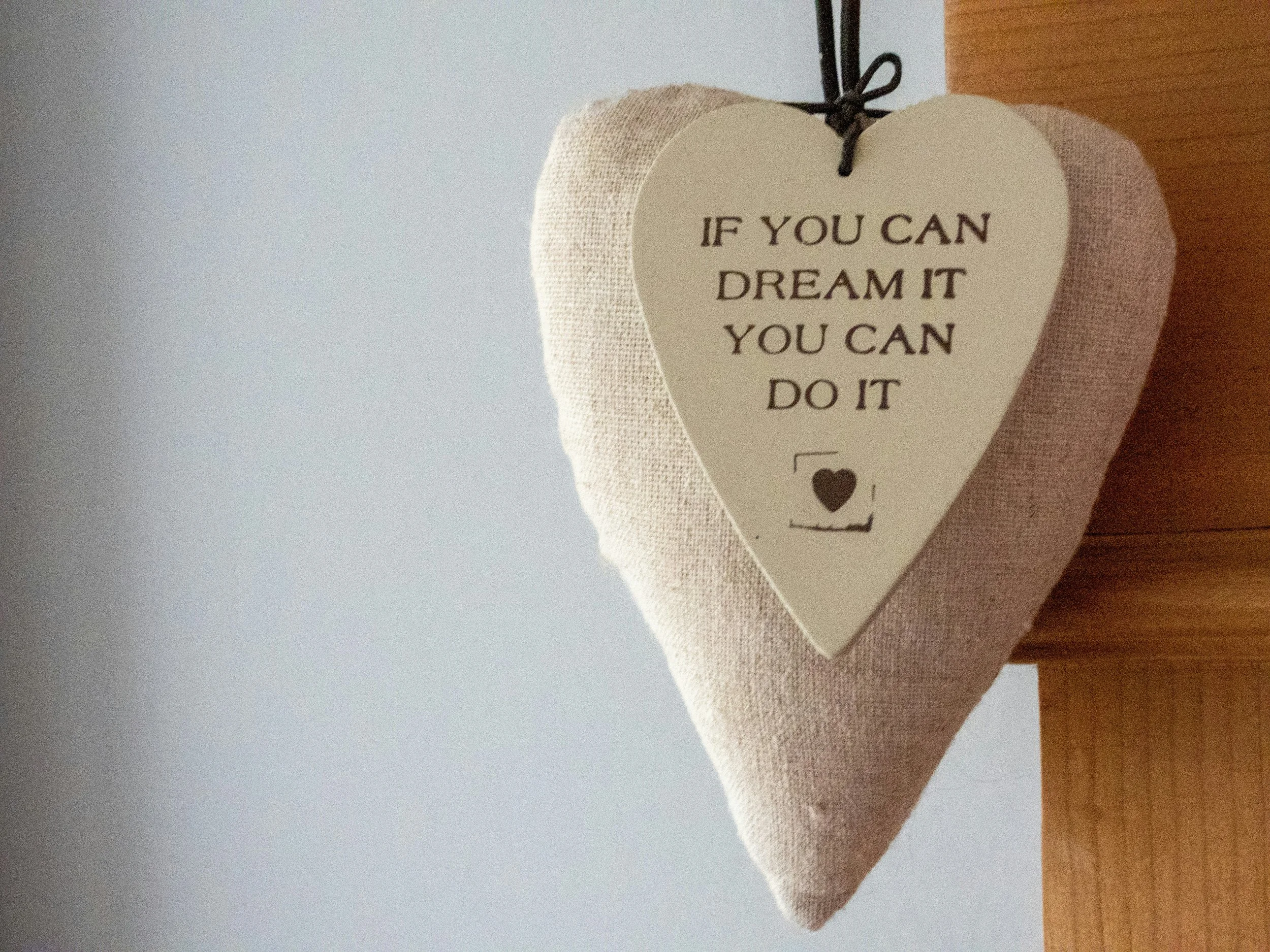 A beige heart-shaped tag on a heart shaped pillow with the motivational quote 'If you can dream it you can do it'.