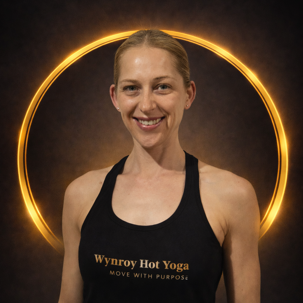 A woman smiling in front of a black background with a glowing gold circle behind her head. She is wearing a black tank top with orange text that reads 'Wynroy Hot Yoga, Move with Purpose'.