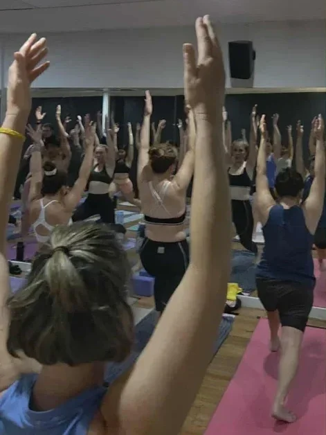 People participating in a yoga or mindfulness class, raising their hands and practicing poses in a studio.