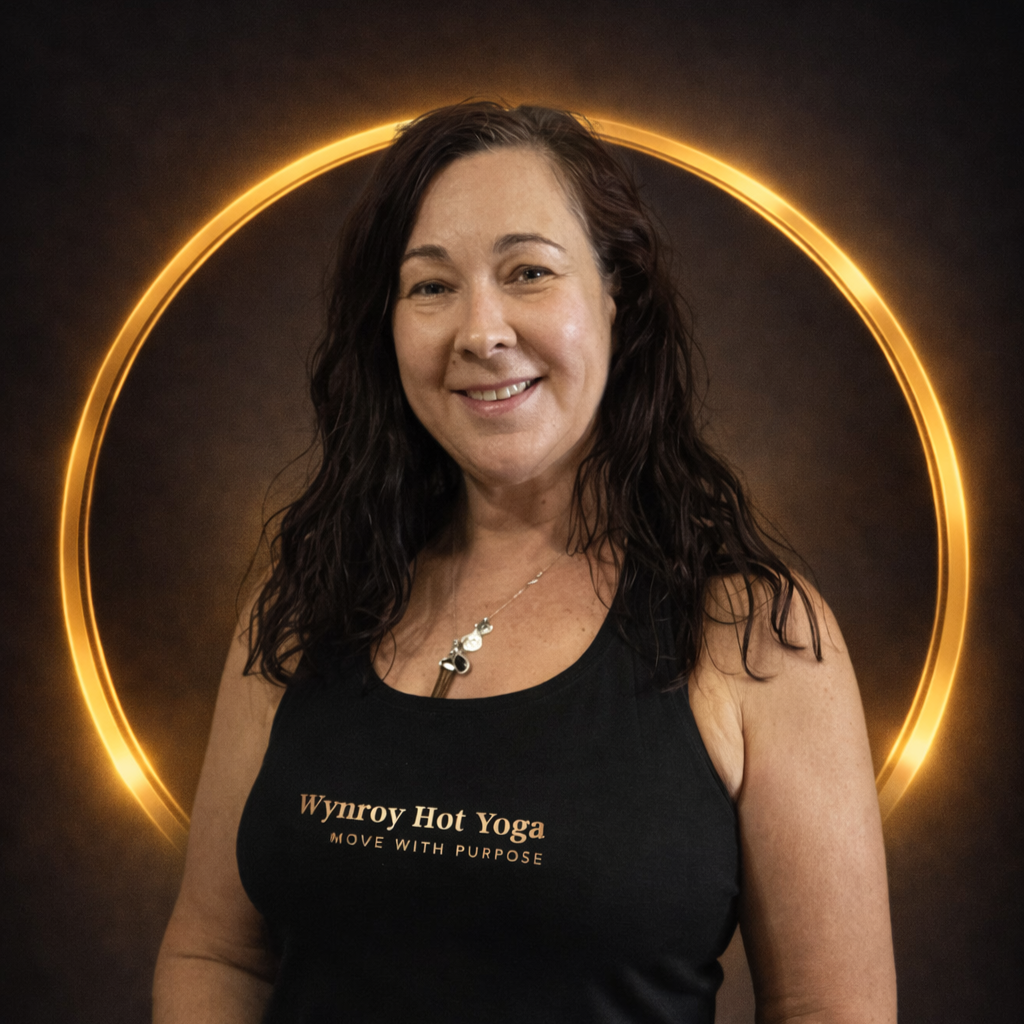 A woman with long dark wavy hair smiling at the camera, wearing a black tank top with the words "Wynroy Hot Yoga" and "Move with Purpose" printed on it, standing in front of a glowing golden circle on a dark background.