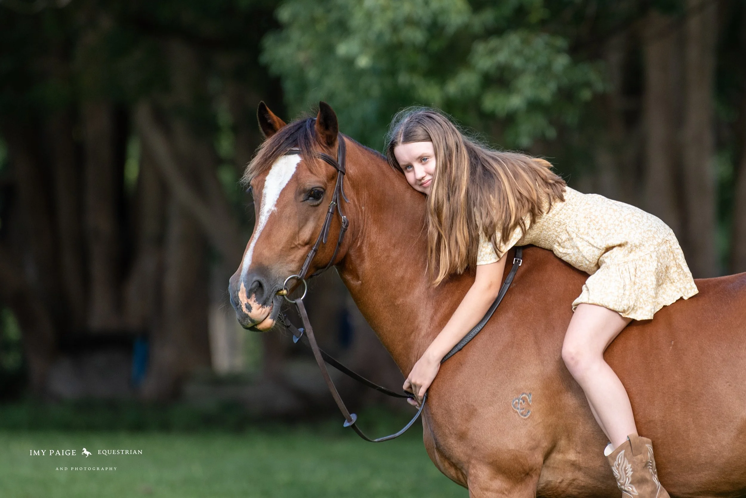 A girl in a yellow dress with long brown hair riding a brown horse with a white stripe on its face outdoors.