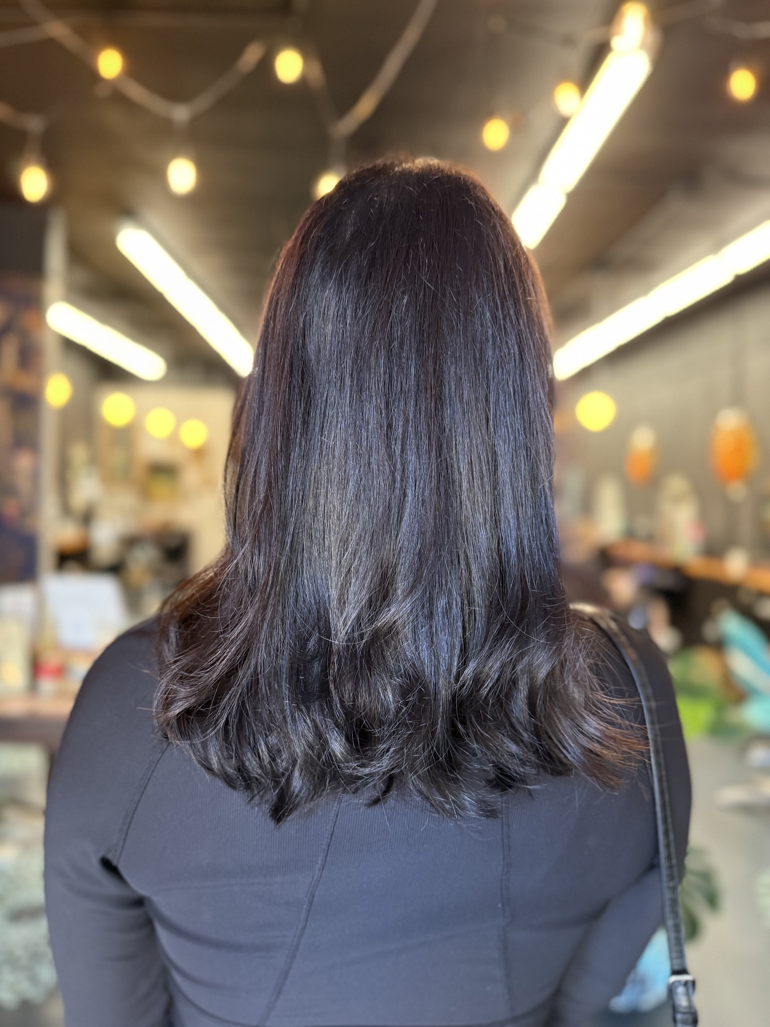 Rear view of person with shoulder-length dark hair in a dimly lit room with string lights.