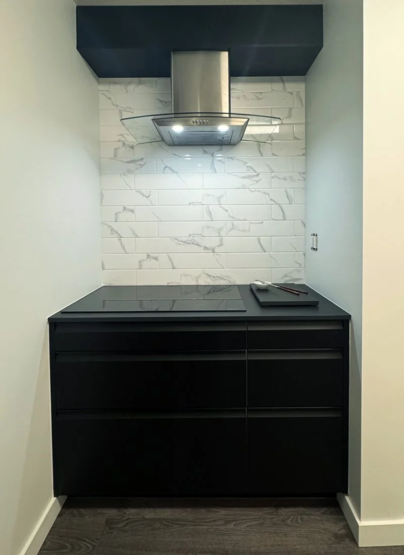 Modern kitchen with a black cabinet, a built-in stove, a stainless steel range hood, and white marble tile backsplash.