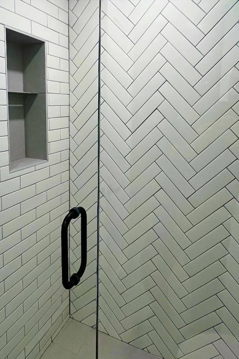 A bathroom shower with white subway tiles and a built-in wall shelf.