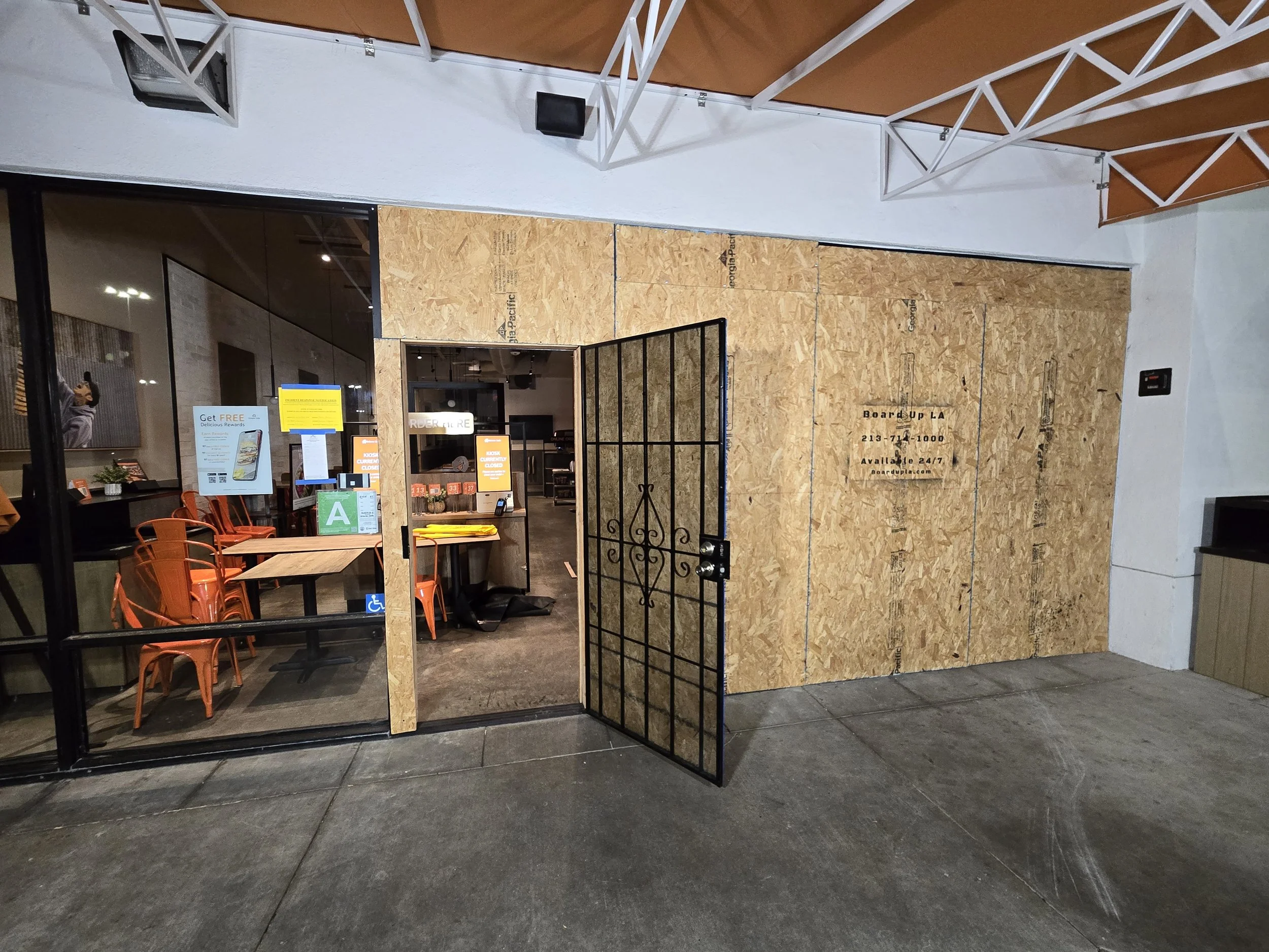 commercial board-up in Los Angeles — plywood securing a 
restaurant storefront with security gate. Indoor emergency service by Boardup LA.