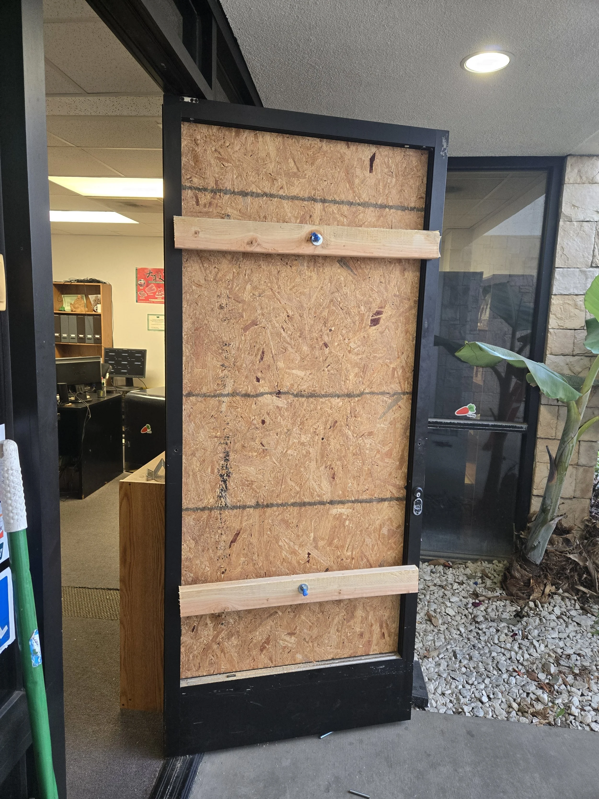 Close-up of a temporary board-up in a doorway, featuring an OSB panel with two visible wooden cross-supports.