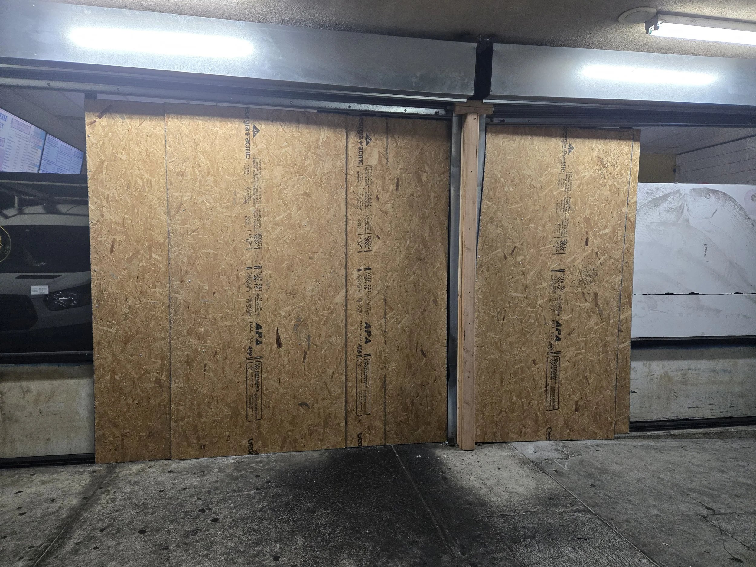 A practical board-up solution: two vertically oriented plywood sheets filling an opening, supported by a heavy-duty overhead beam.