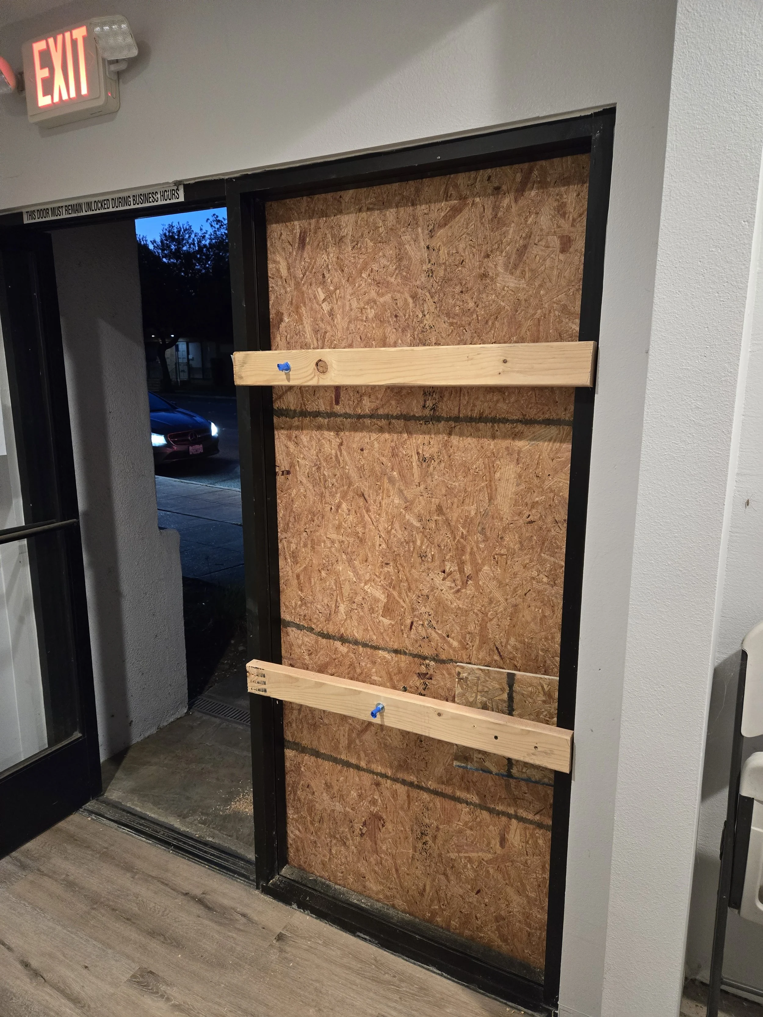 Indoor view of a temporary door board-up, featuring an OSB panel with two horizontal wooden supports.
