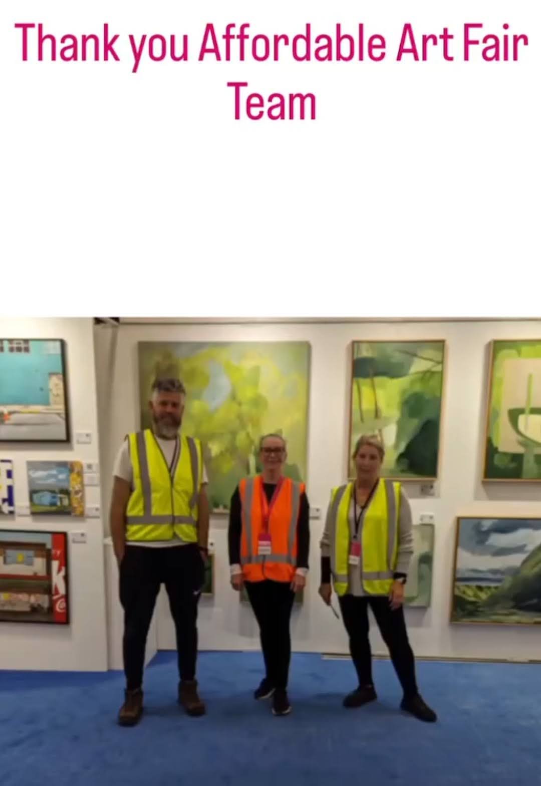 Group of three people wearing high visibility vests standing in front of artwork at an art fair.