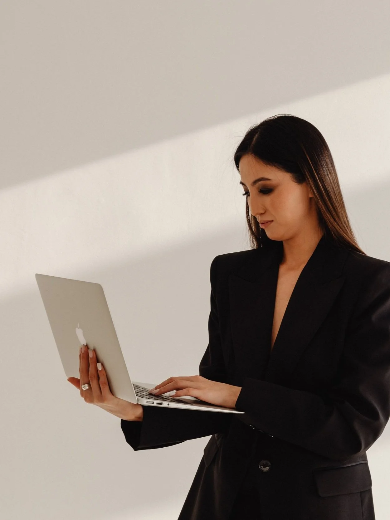 Woman in a black suite typing on a laptop standing against a white background