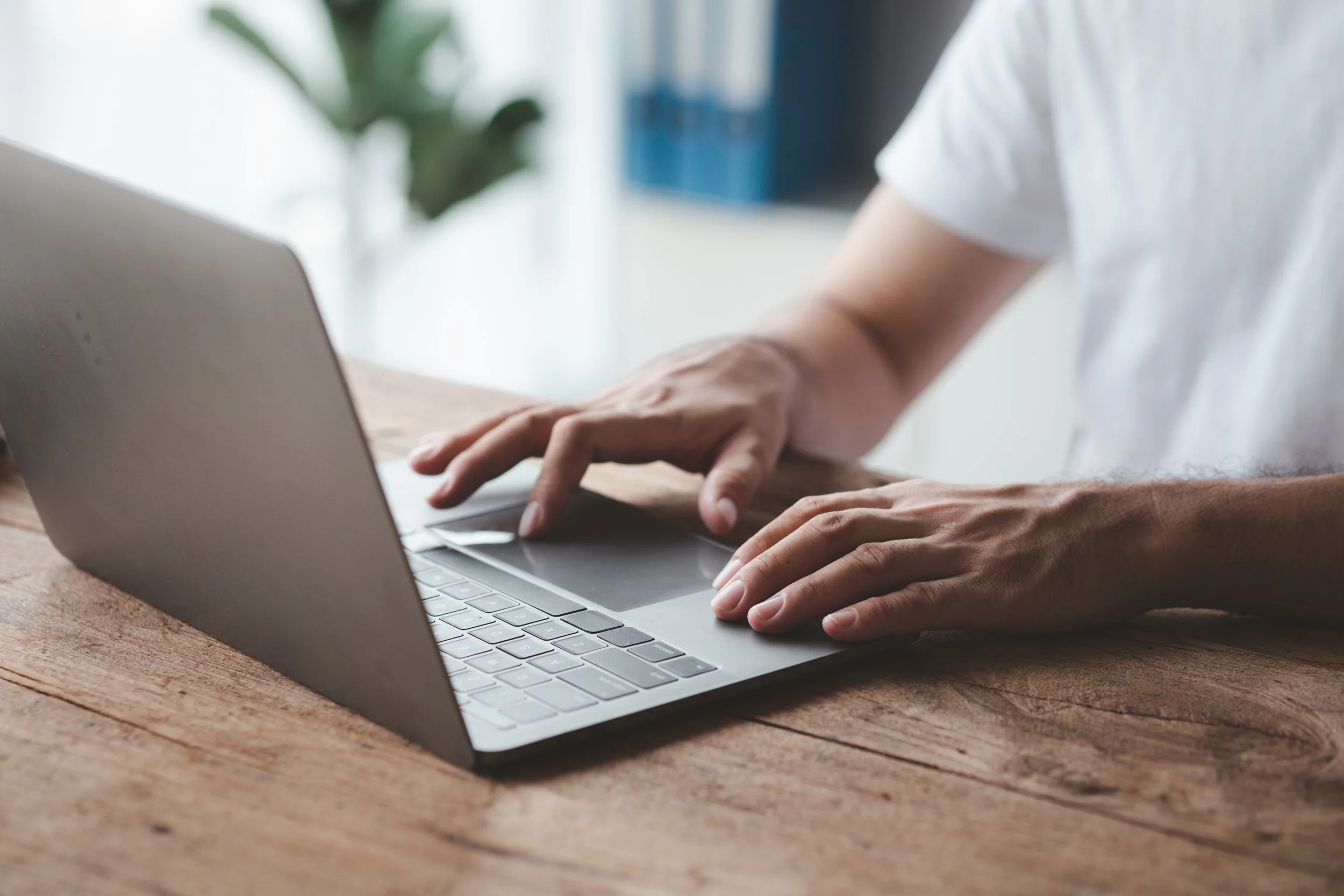 A person typing on a silver laptop placed on a wooden table.