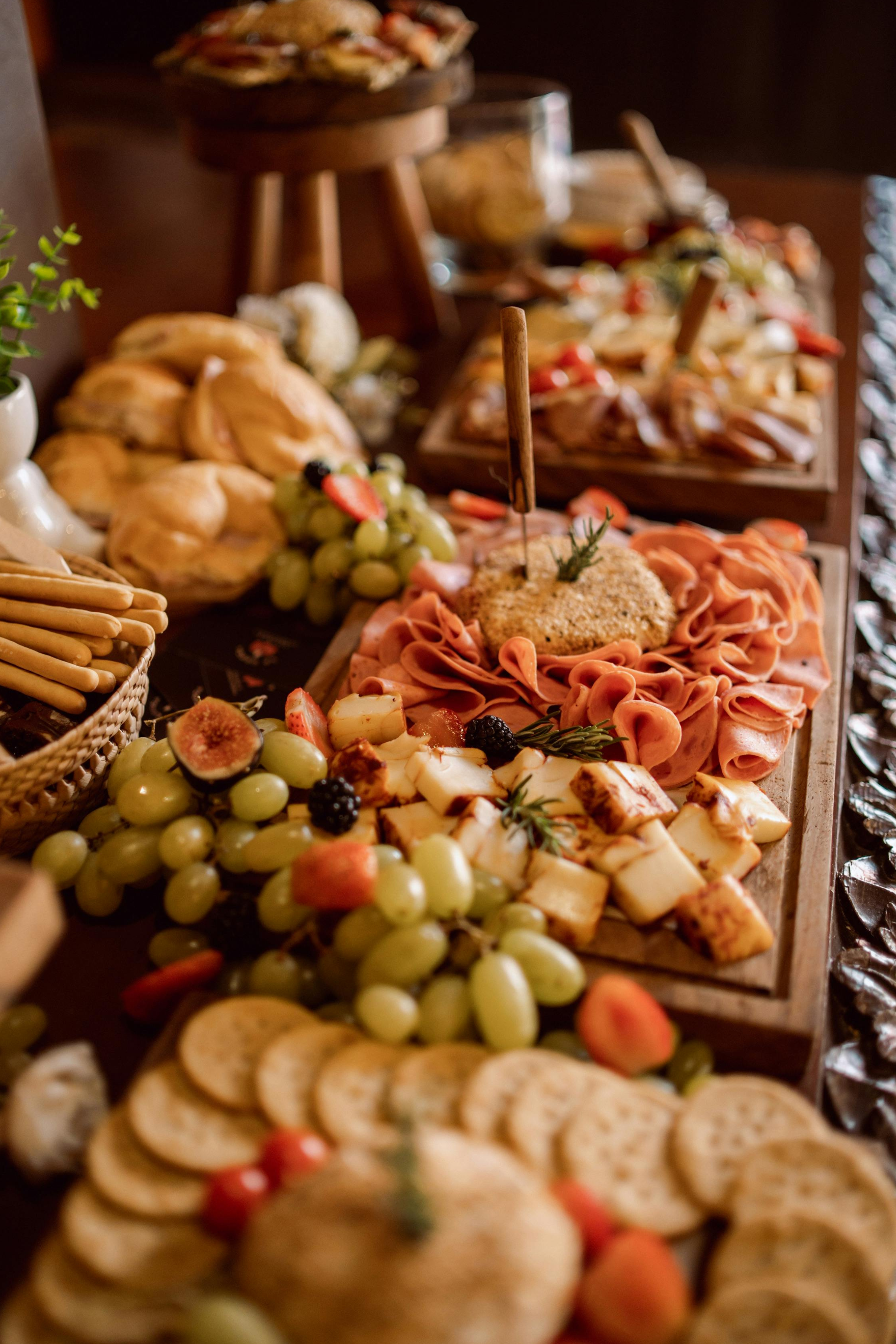 A spread of assorted appetizers including cheeses, grapes, sliced meats, bread, and crackers on a wooden table.