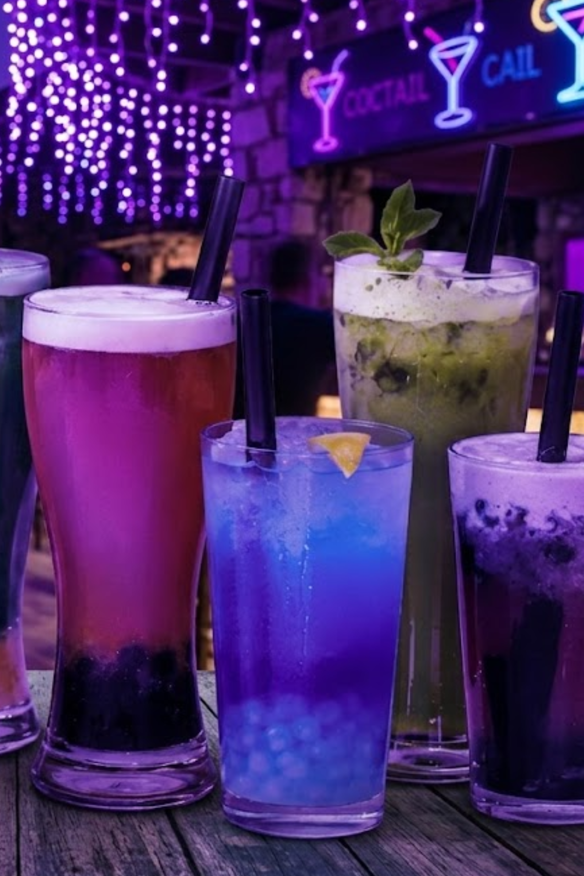 A variety of colorful cocktails on a wooden table near a background with purple neon lights and signs for cocktails and calling.