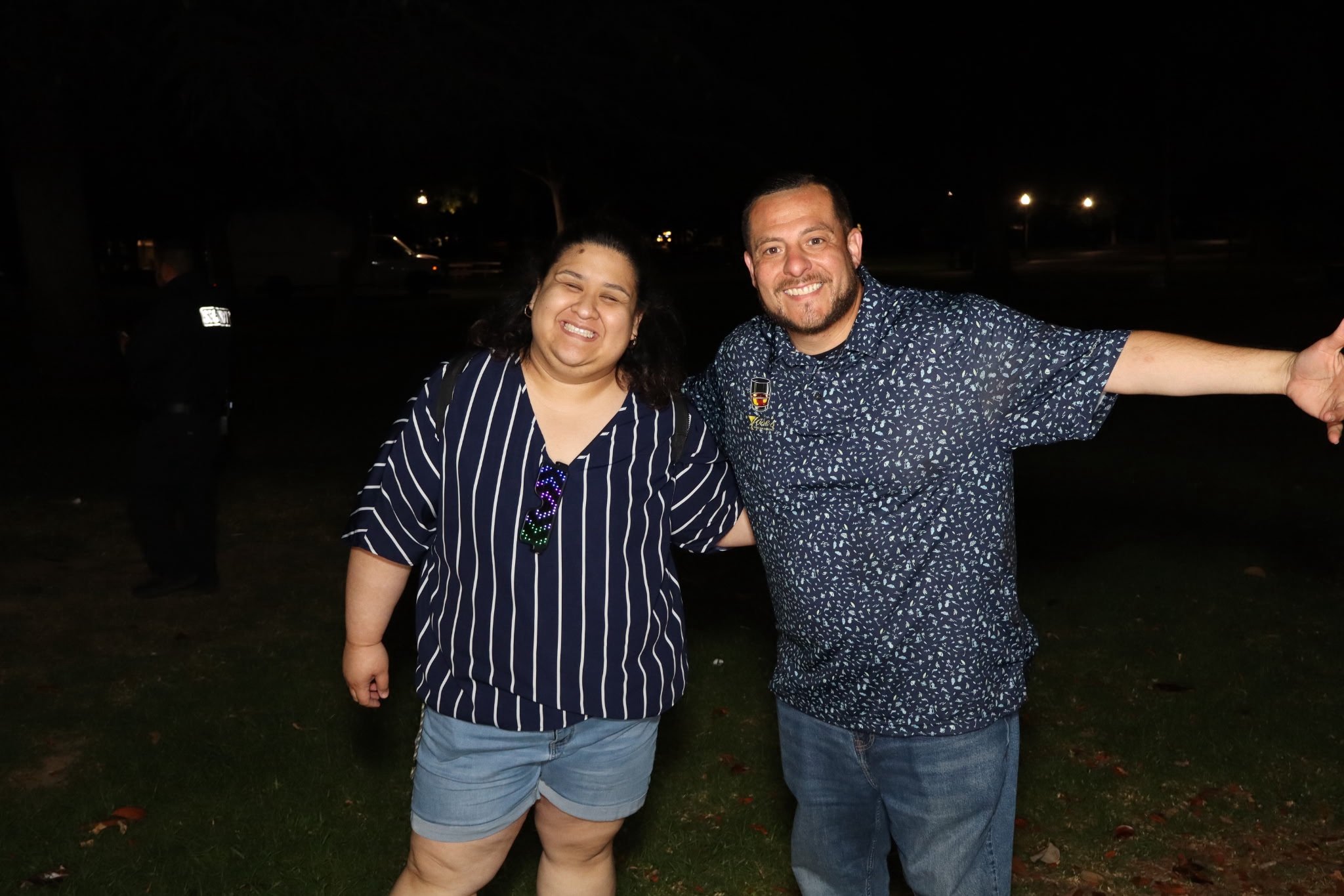 A woman with dark curly hair smiling and a man with short hair and a beard smiling, standing outdoors at night.
