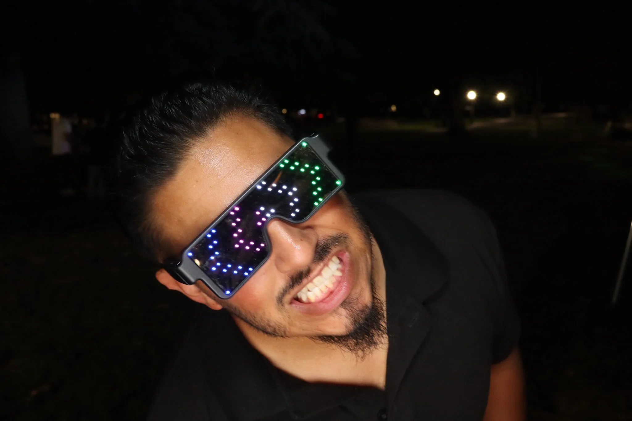 A man smiling laughing at night, wearing LED glasses with colorful lights.