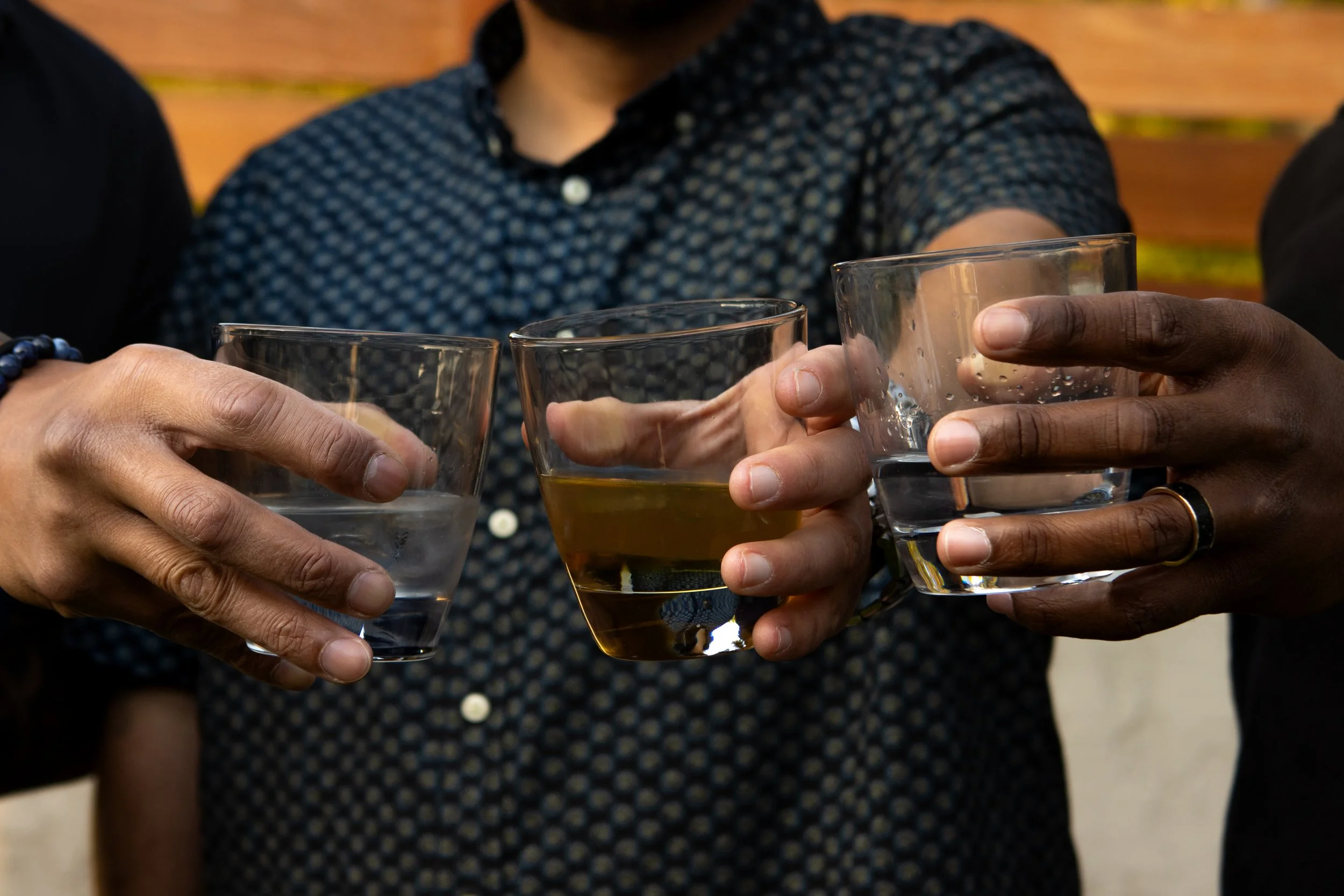 Group of people holding glasses with drinks, clinking them together in a toast outdoors.