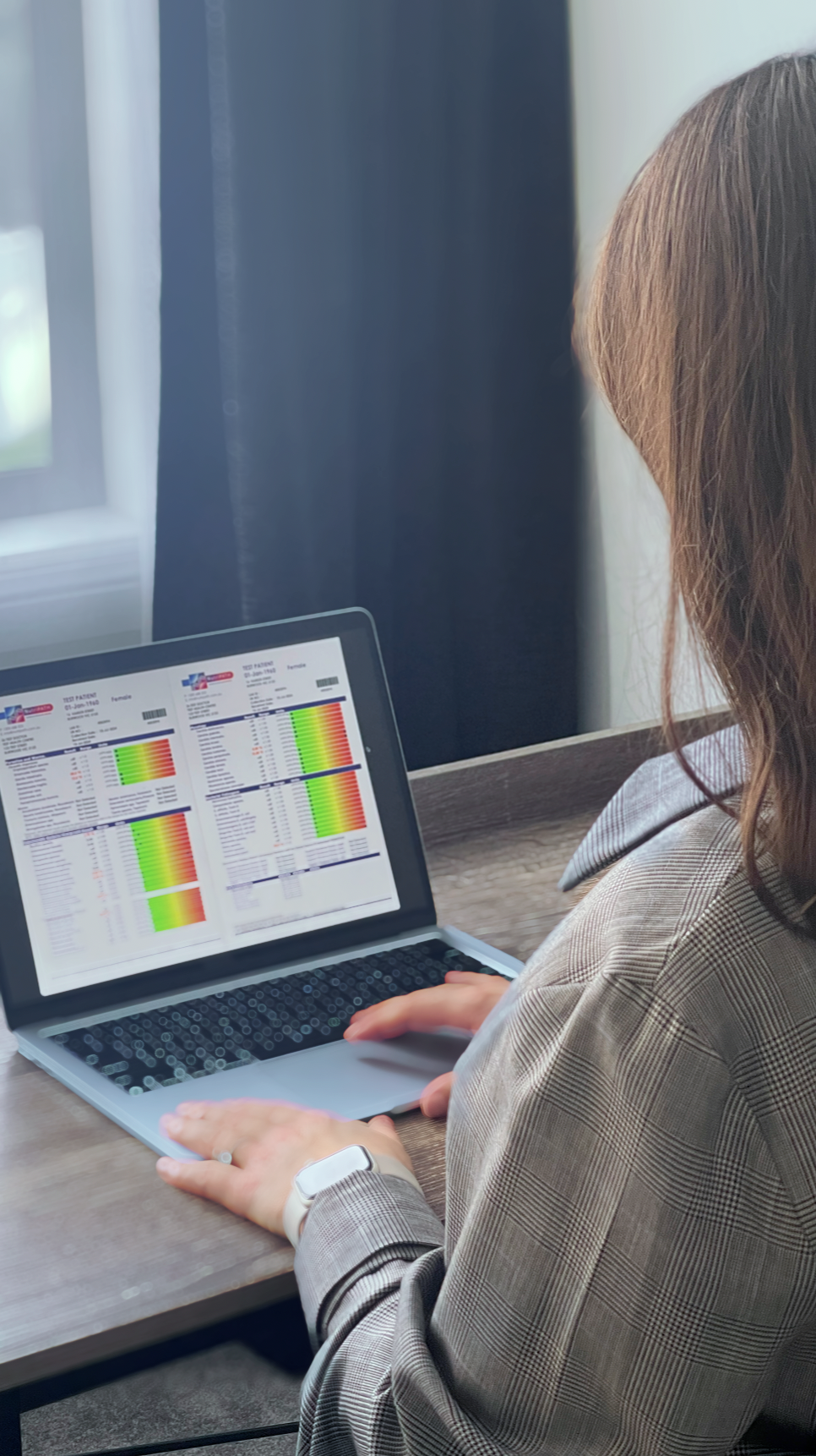 Person working on a laptop displaying a graph on stress levels, seated at a desk with potted plants in the background near a window.