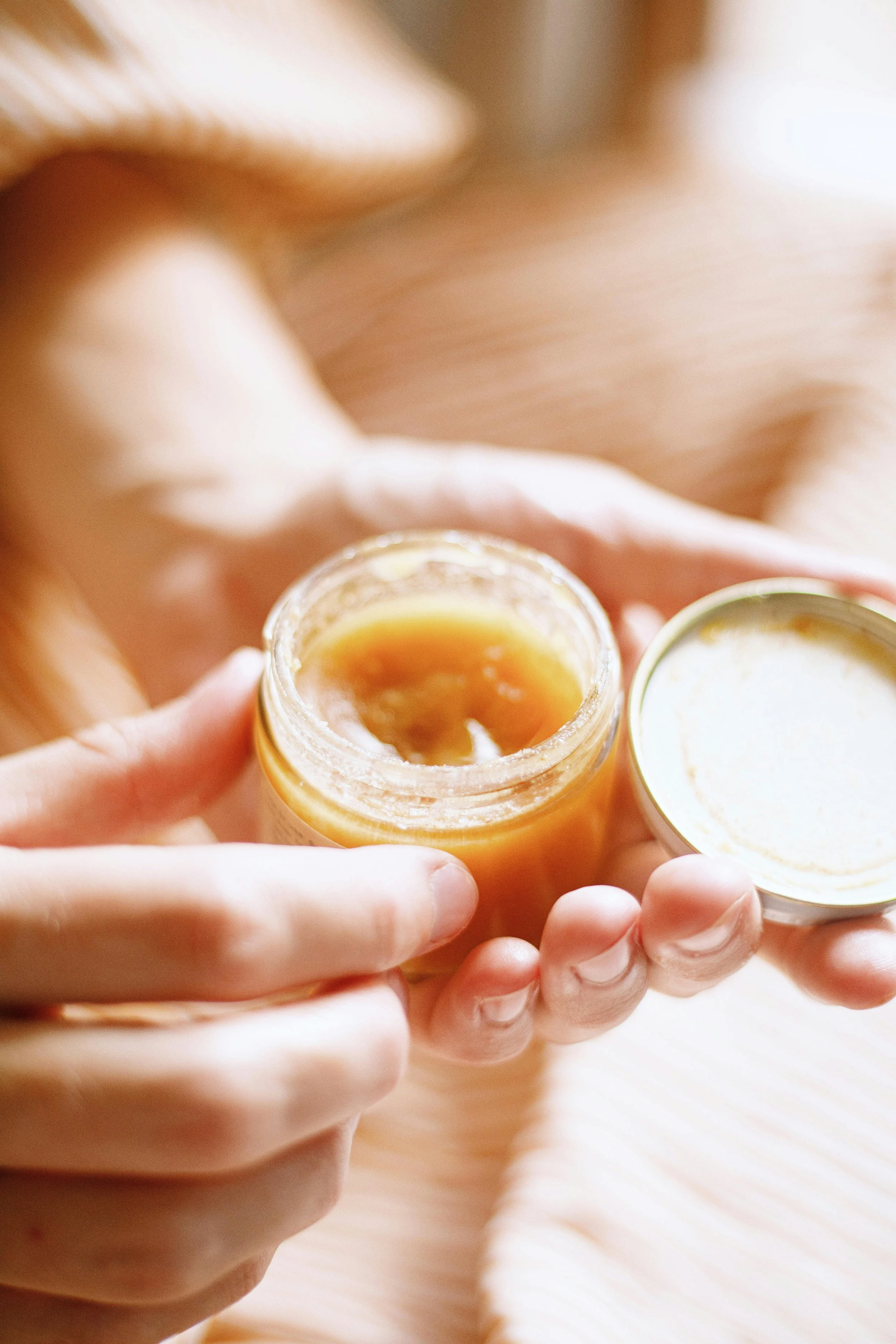 Close-up of person holding a jar of honey with the lid removed, revealing honey inside.