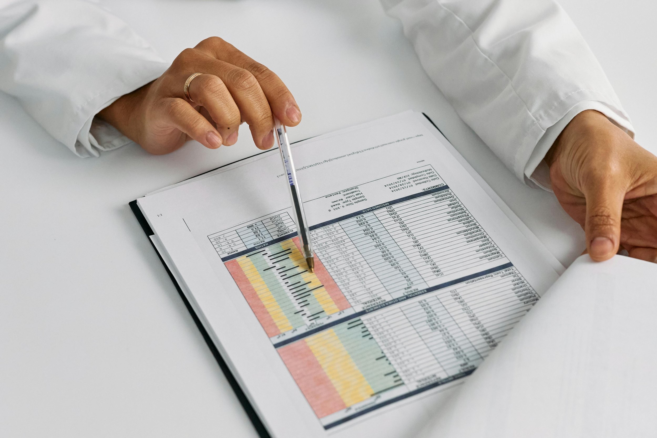 Person in white coat analyzing a printed lab report or scientific data with a pen.
