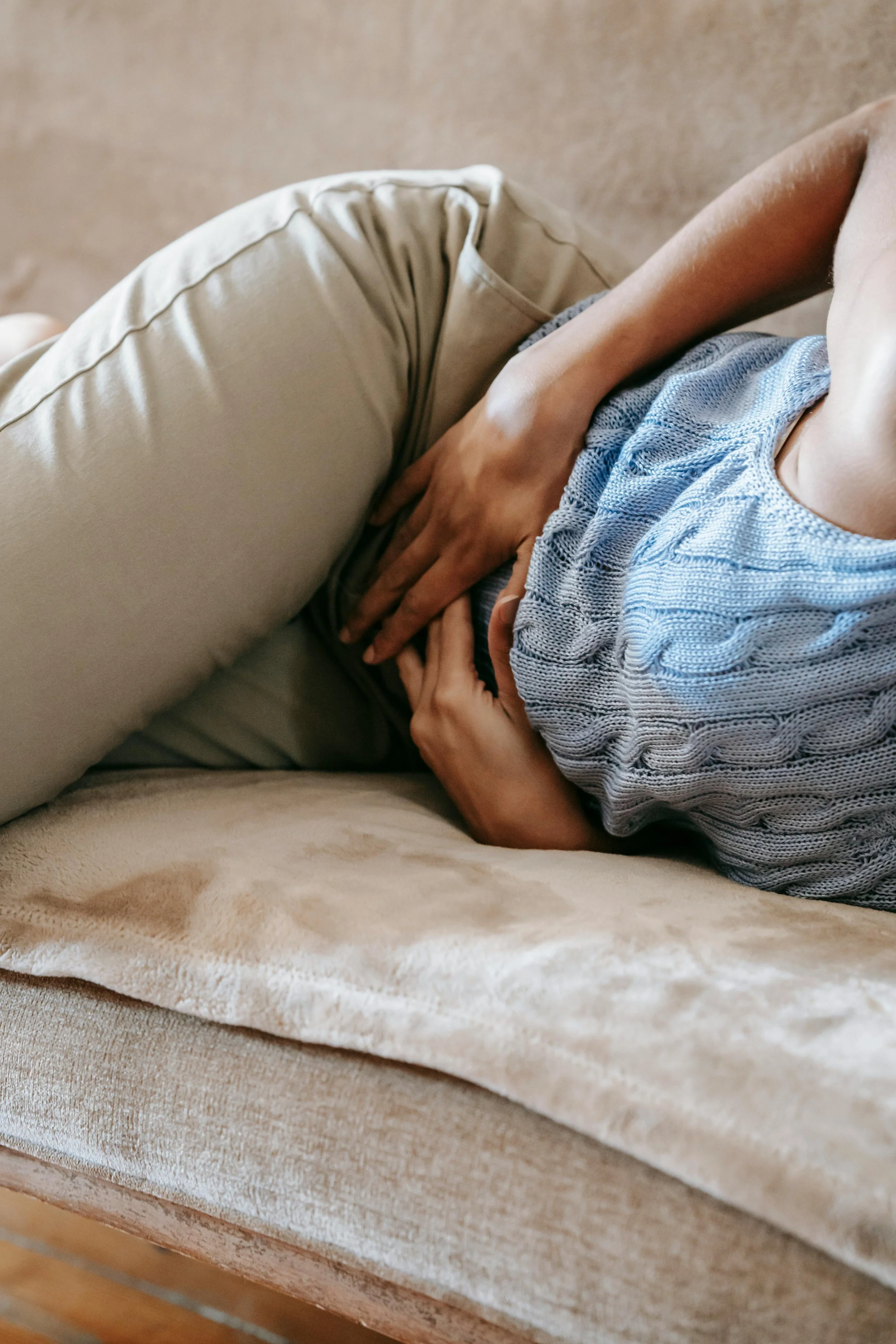 Person lying on a sofa, clutching their stomach, appearing to be in pain.