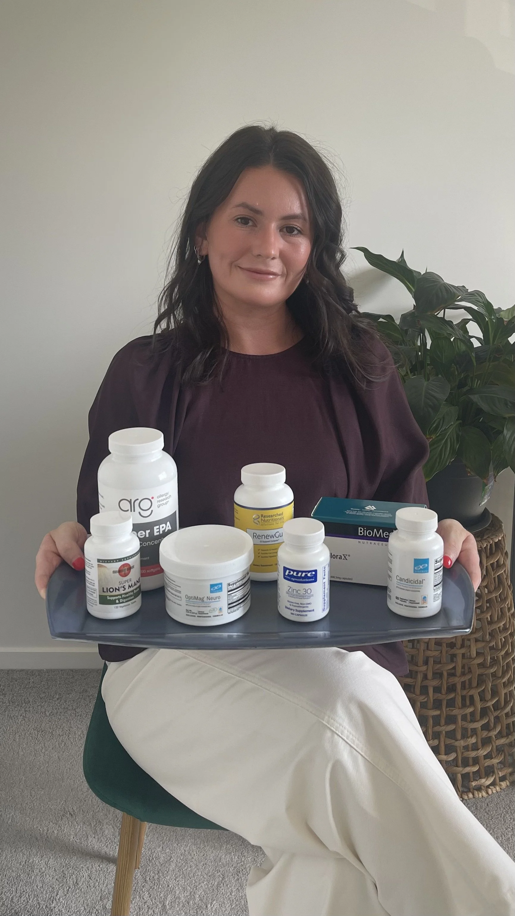 A woman sitting on a green chair holding a tray with various supplement bottles and boxes.