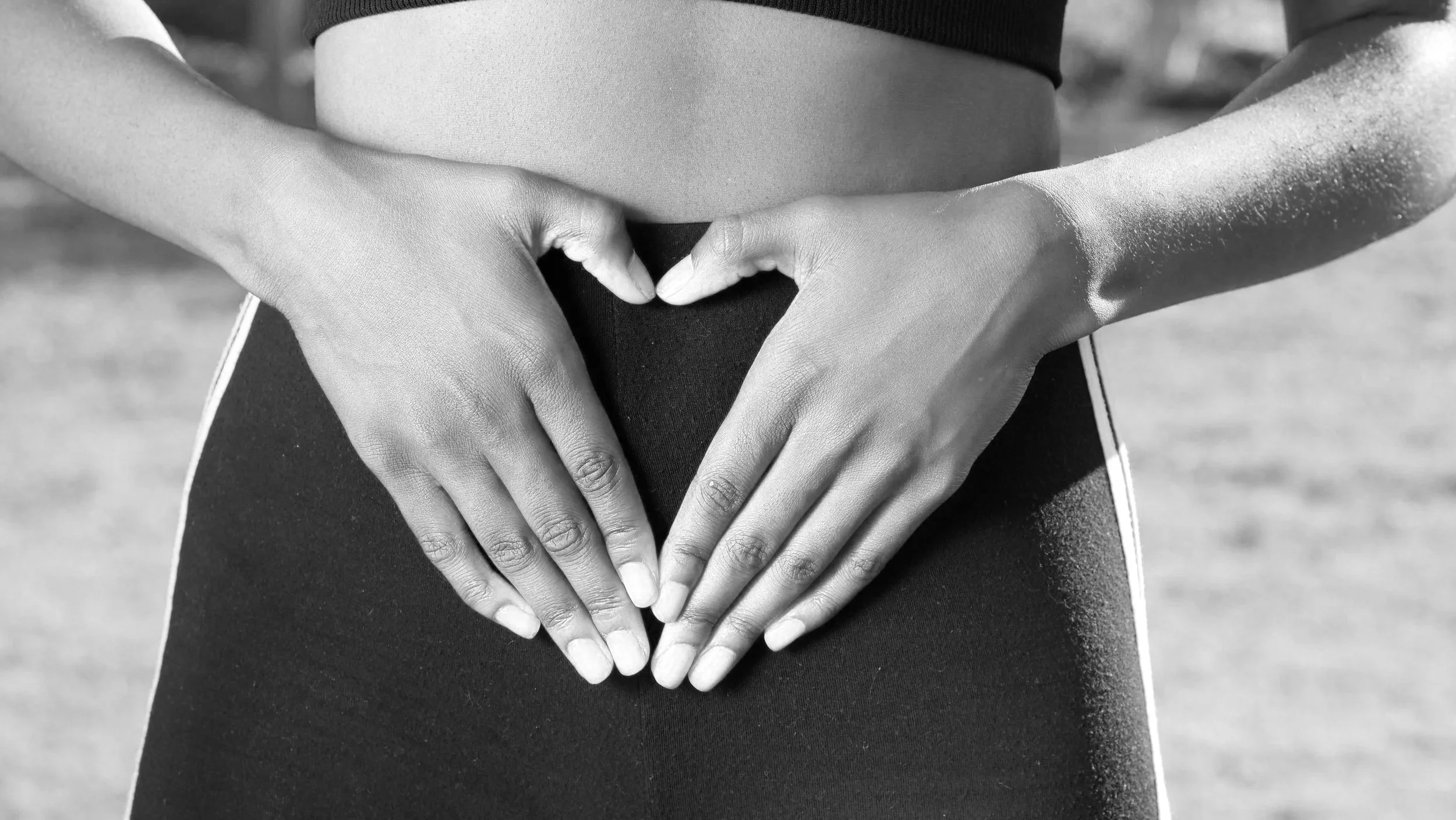 A person making a heart shape with their hands over their stomach in black and white.