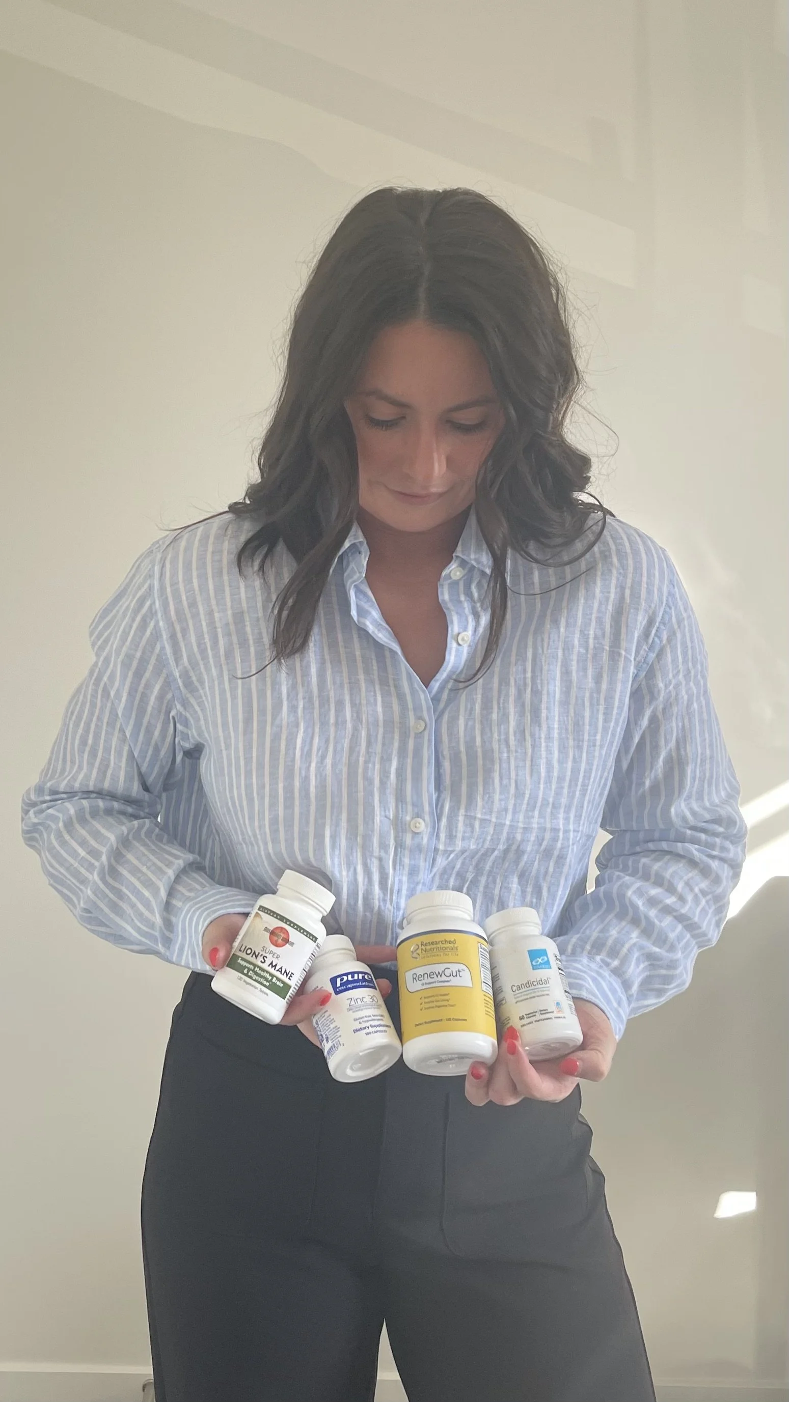 Dr Adriela from 'Future You Wellness' - 'Functional Medicine' with dark wavy hair wearing a light blue striped shirt holding various supplement bottles.
