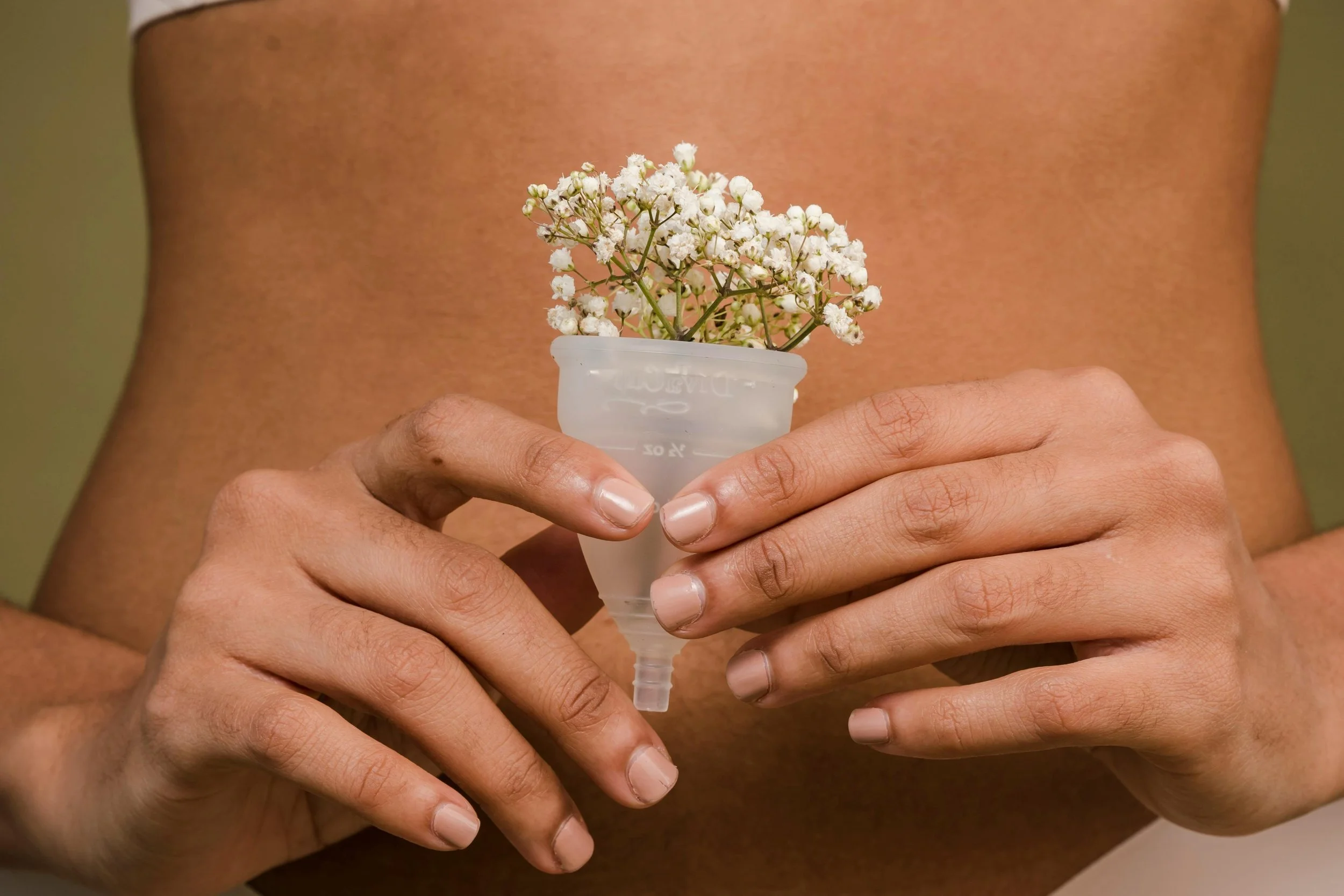 Person holding a small transparent cup with white flowers inside, bare chest visible in the background.