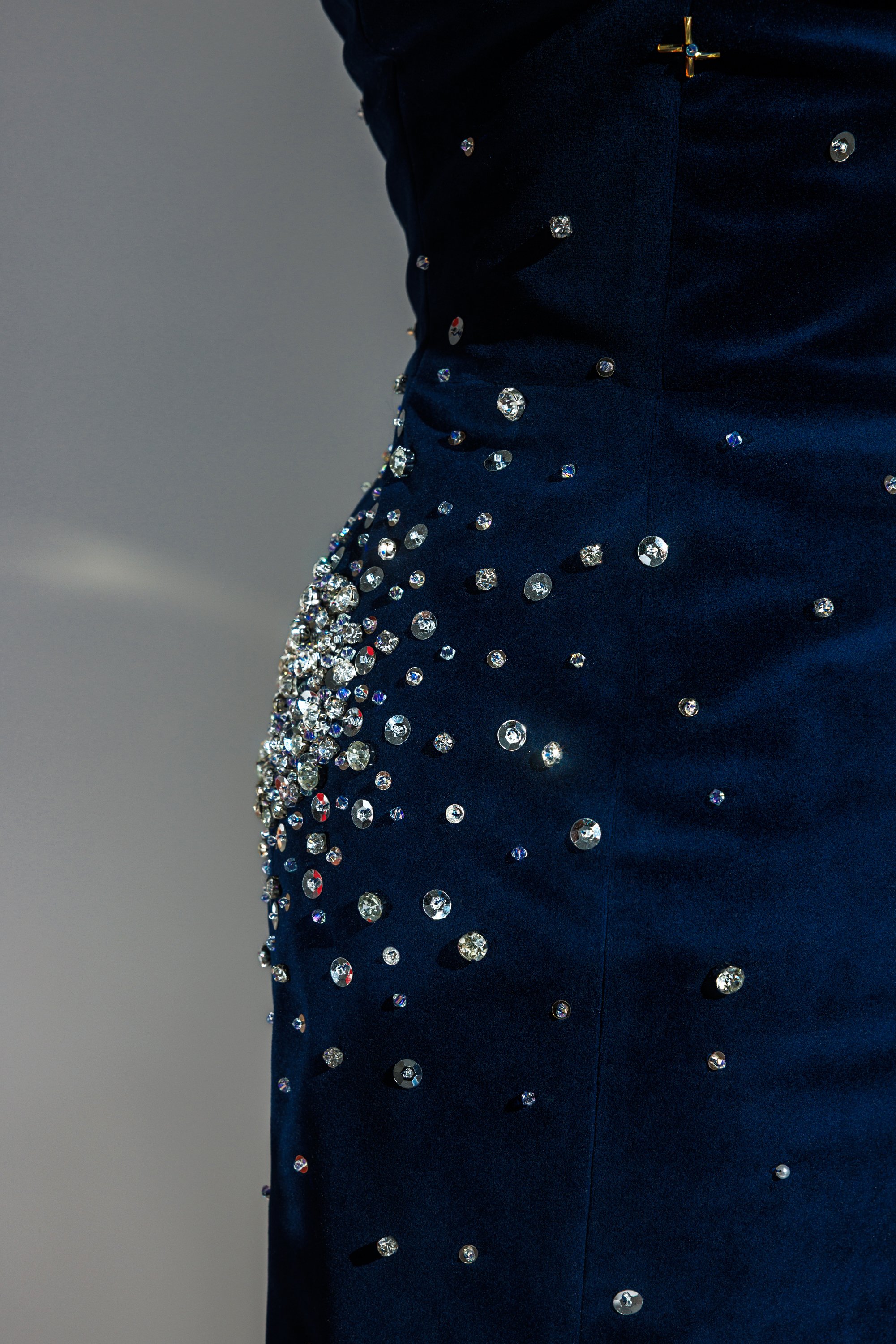 Close-up of a dark blue fabric embellished with scattered rhinestones and a small gold cross pin.