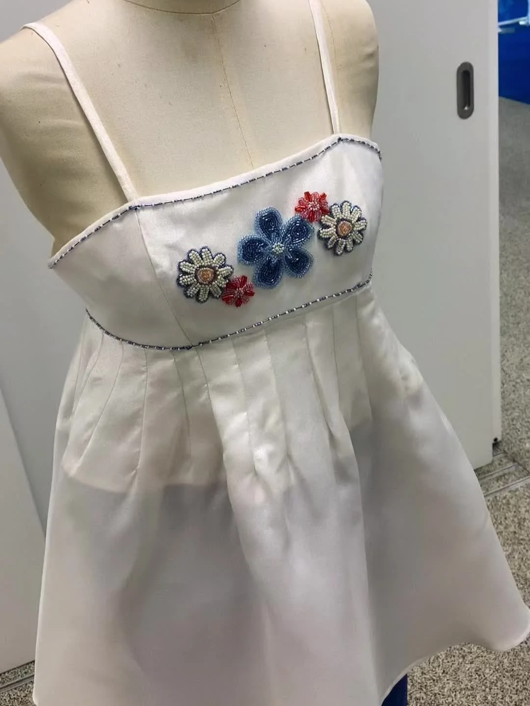 A white satin dress with embroidered floral design on the bodice displayed on a mannequin.