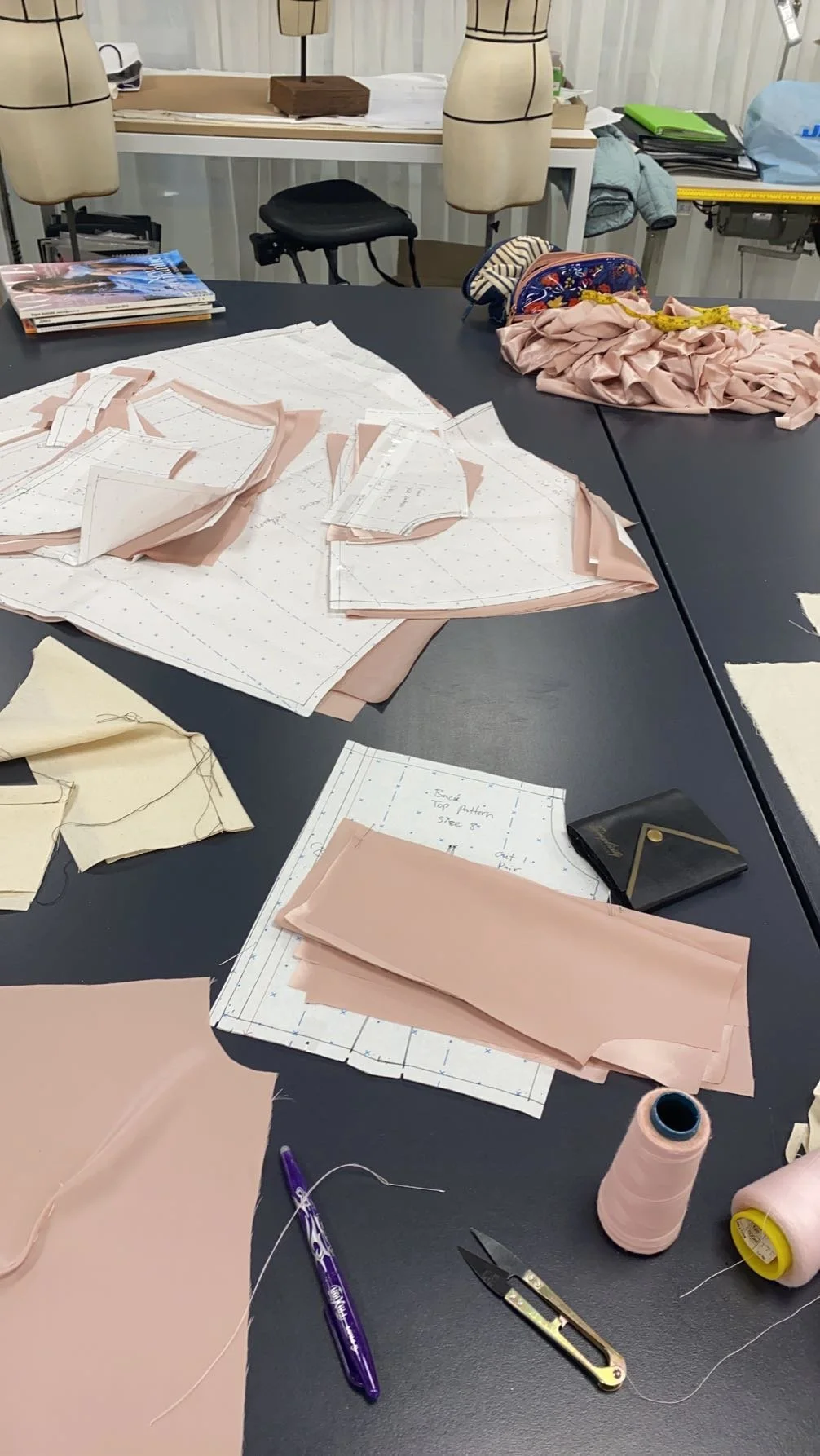 Pattern-making workspace with fabric pieces, sewing patterns, scissors, thread, and notes on the table.