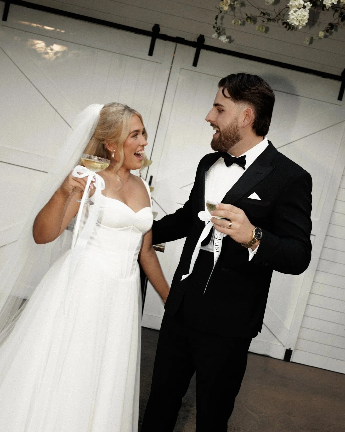 A bride and groom celebrating at their wedding reception, holding glasses of champagne and smiling at each other.