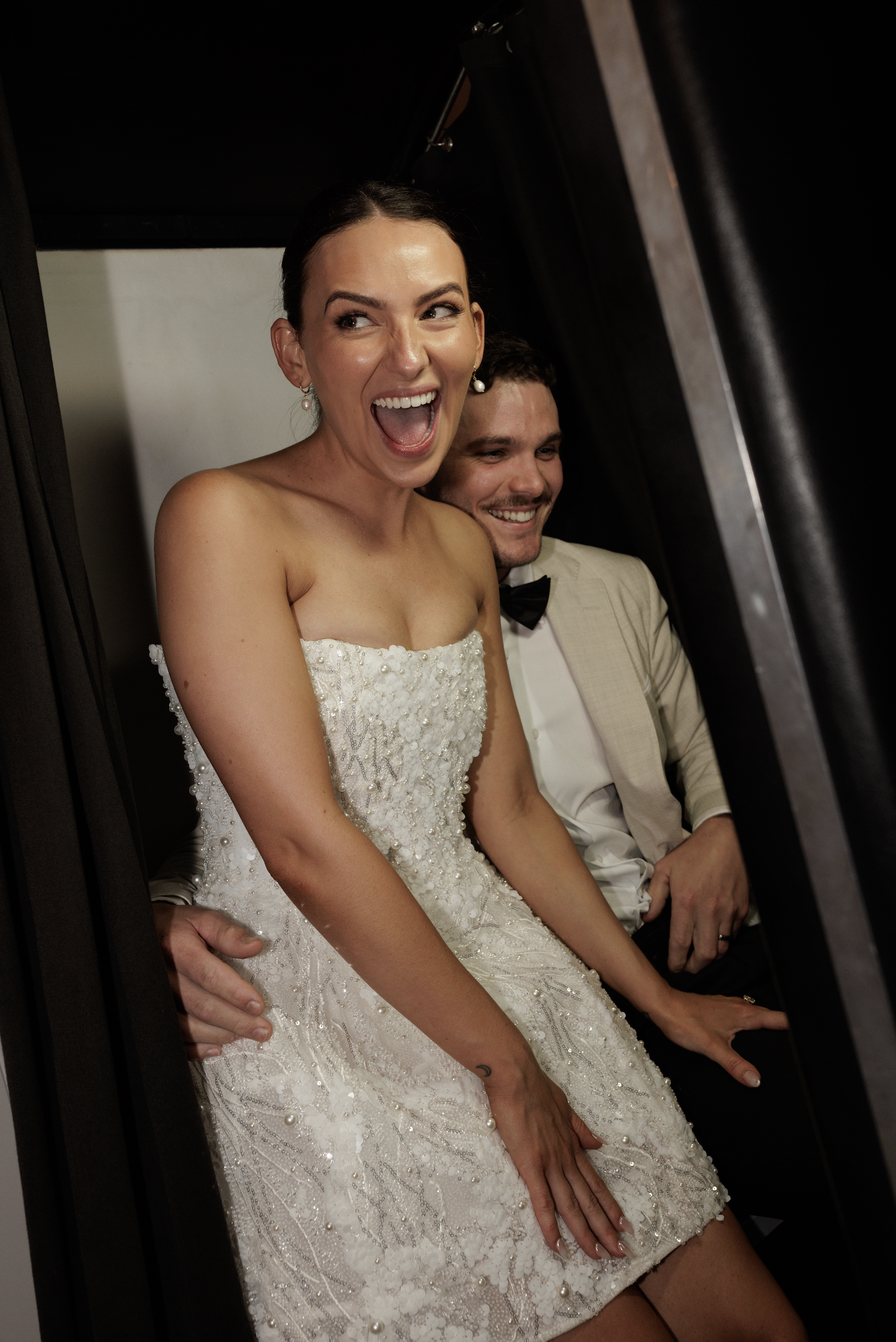 A woman in a wedding dress and a man in a suit are sitting in an elevator, smiling and having fun.