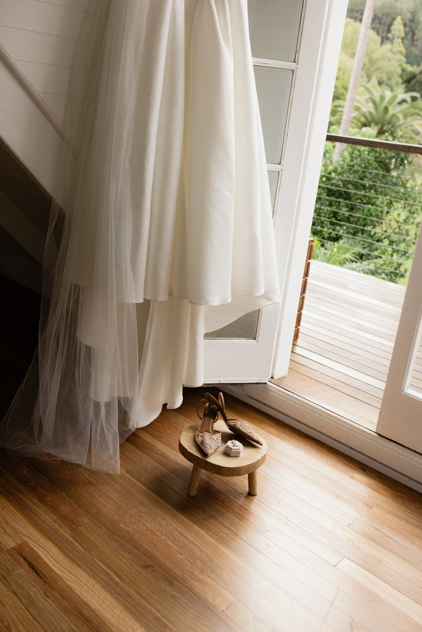 A pair of fancy shoes on a small wooden stool near a door with a view of lush greenery outside.