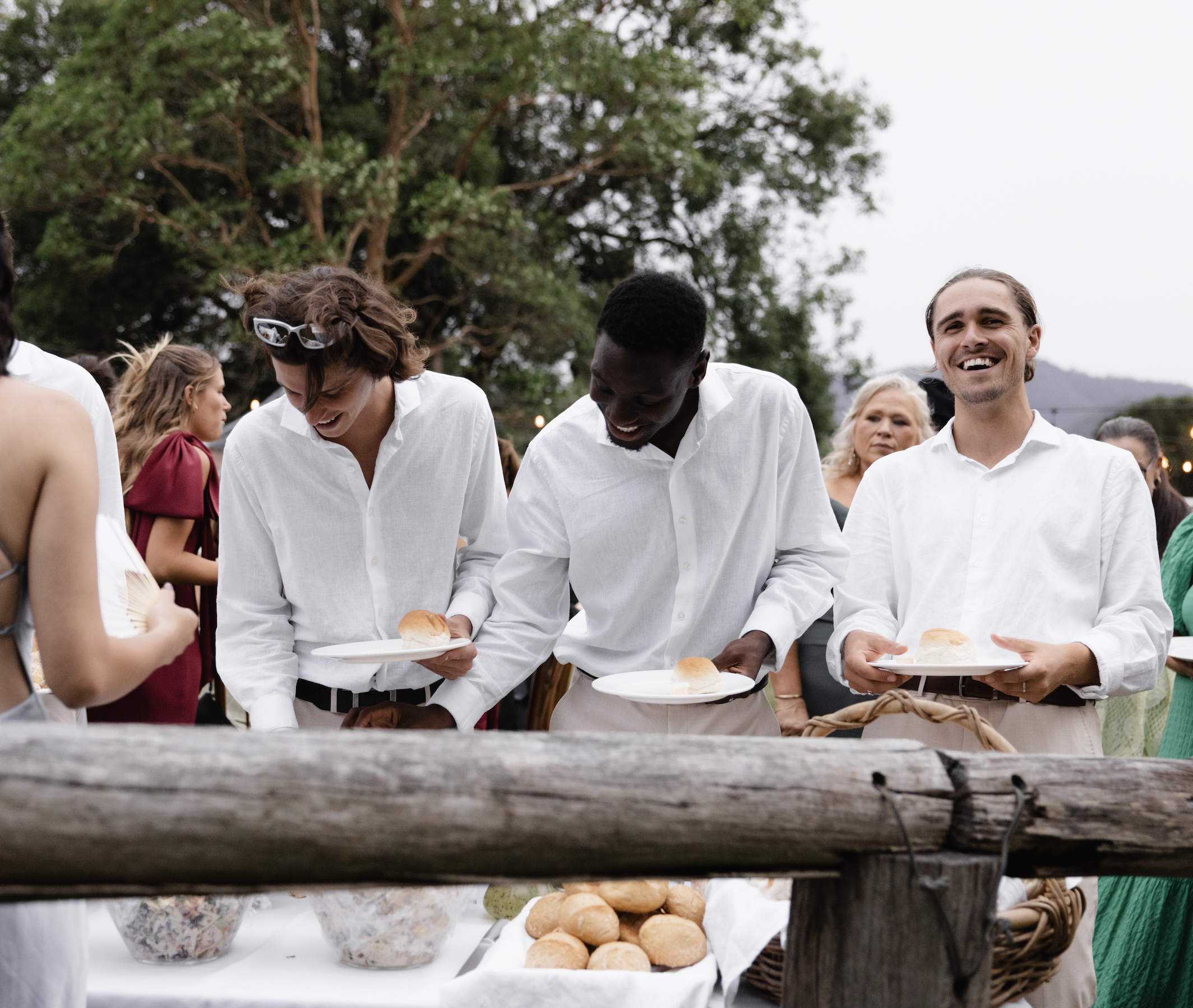 Group of diverse people at an outdoor gathering, serving themselves bread from a buffet table.