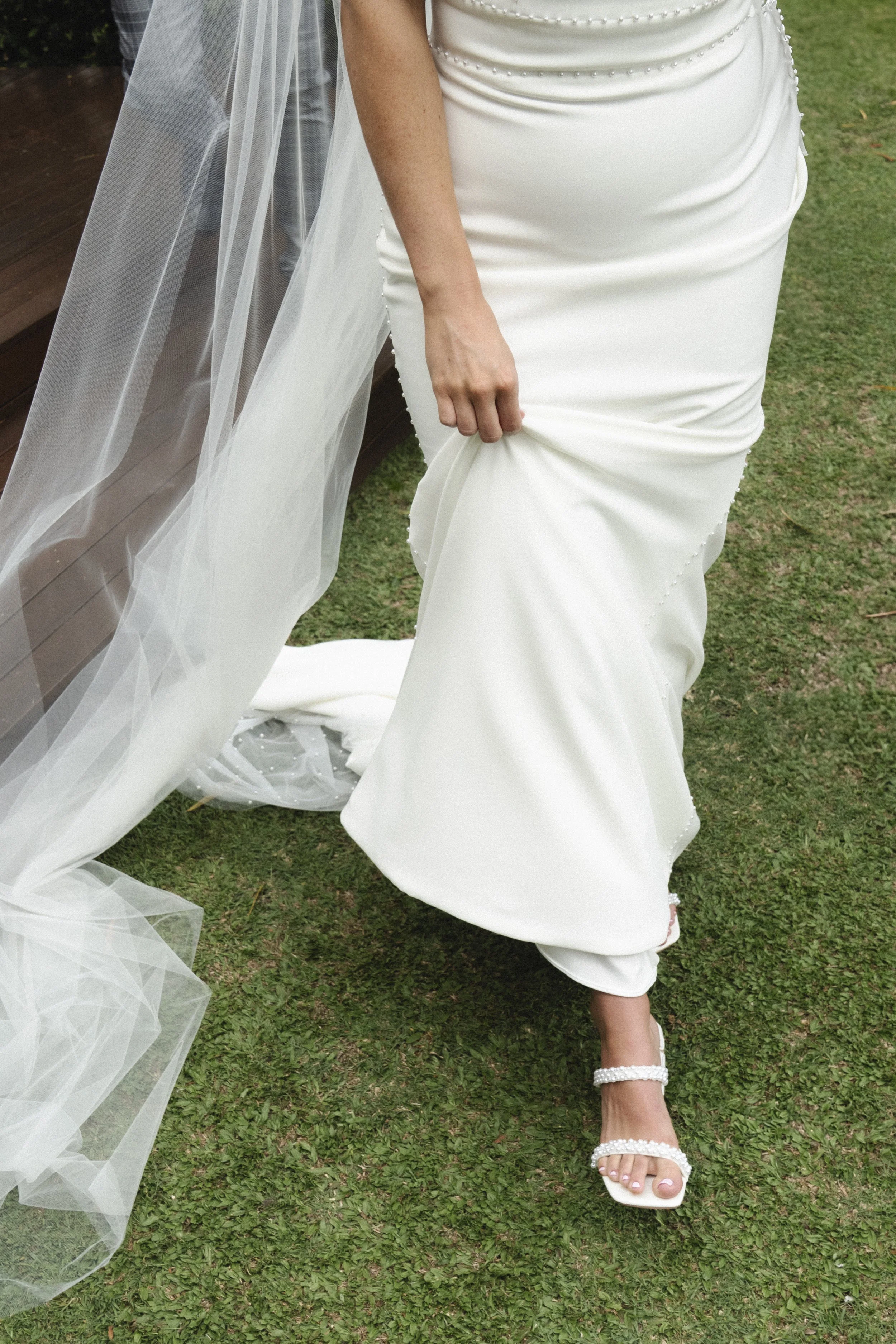 Bride in white dress with veil, holding gown, walking on grass wearing jeweled sandals - Elevated Weddings shot on 35mm film