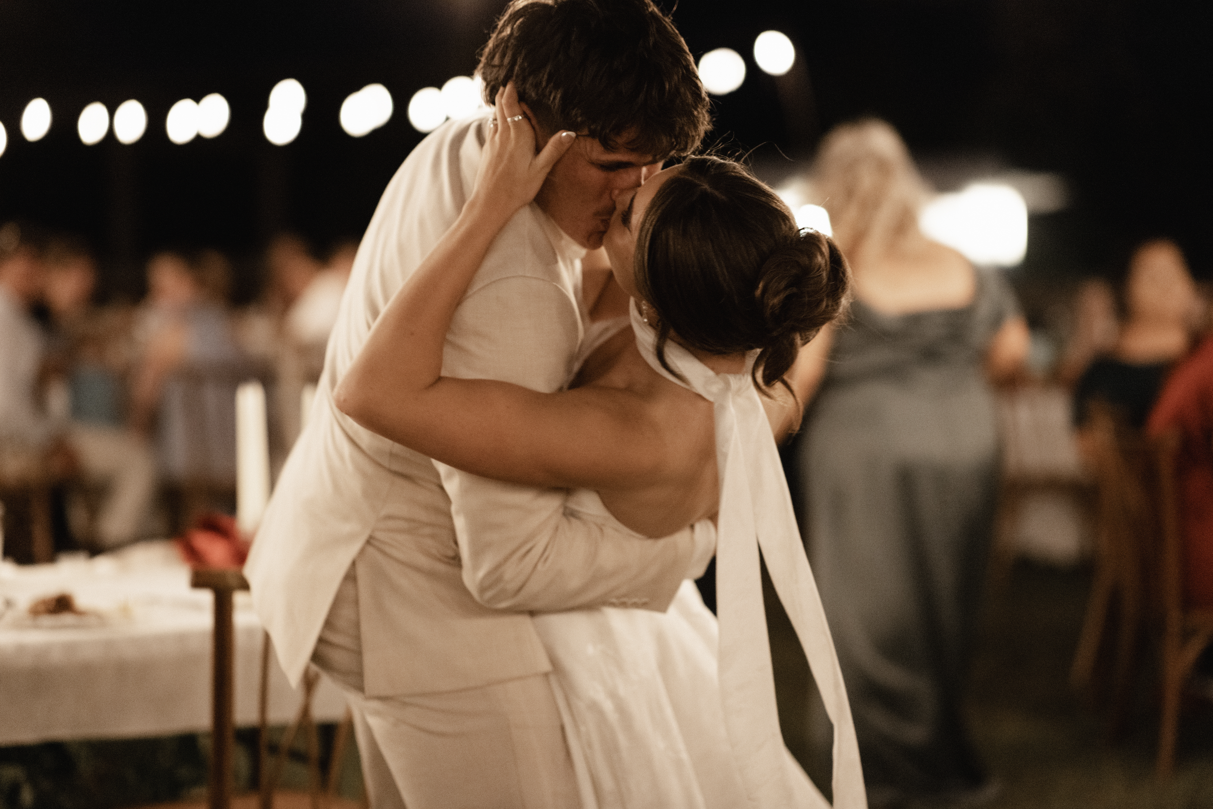 A man and woman are dancing closely at a wedding reception, sharing a romantic moment under warm lighting.