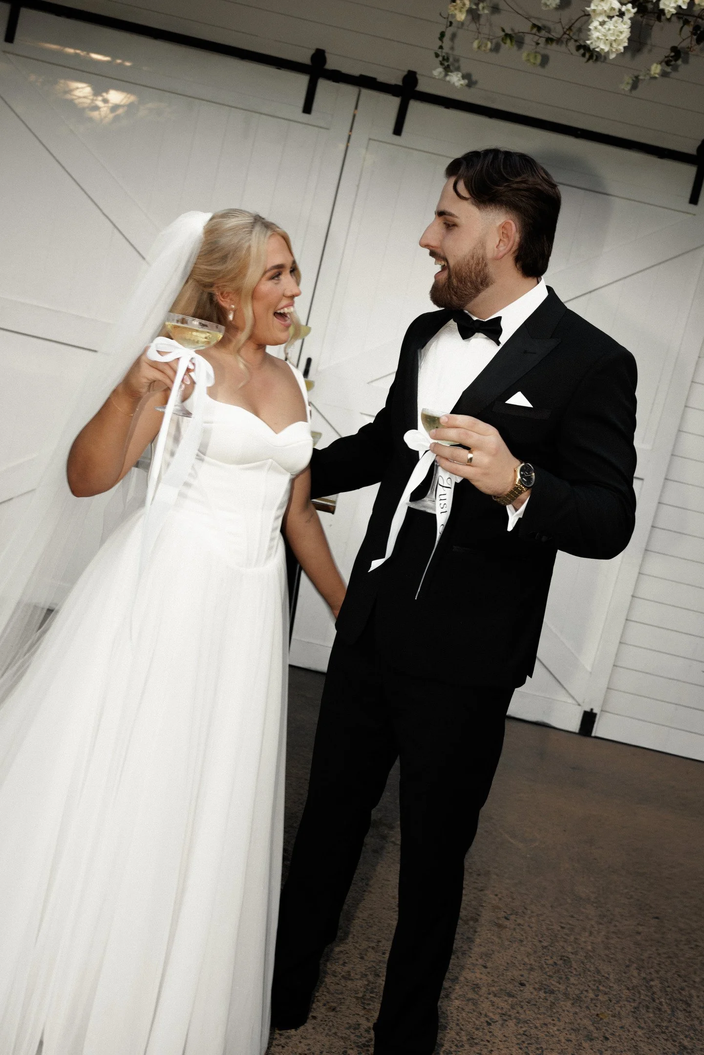 A bride and groom celebrating at their wedding reception, holding glasses of champagne and smiling at each other.
