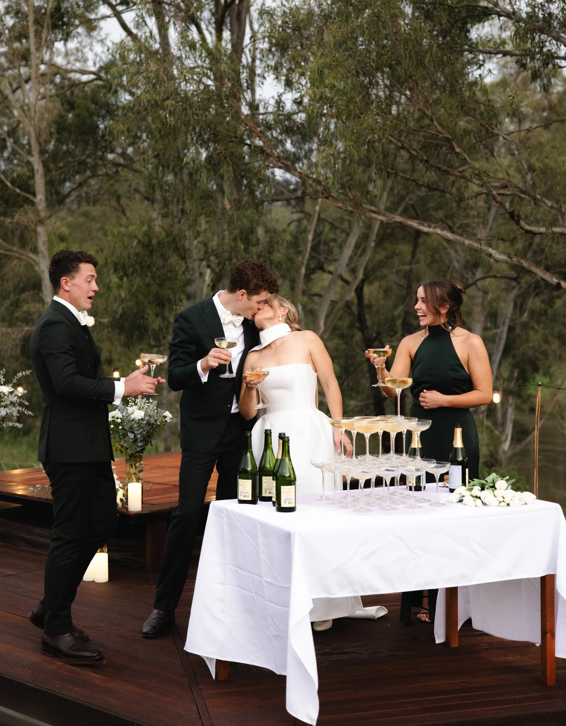 Wedding celebration with bride, groom, and guests around champagne tower on outdoor deck -Elevated Weddings