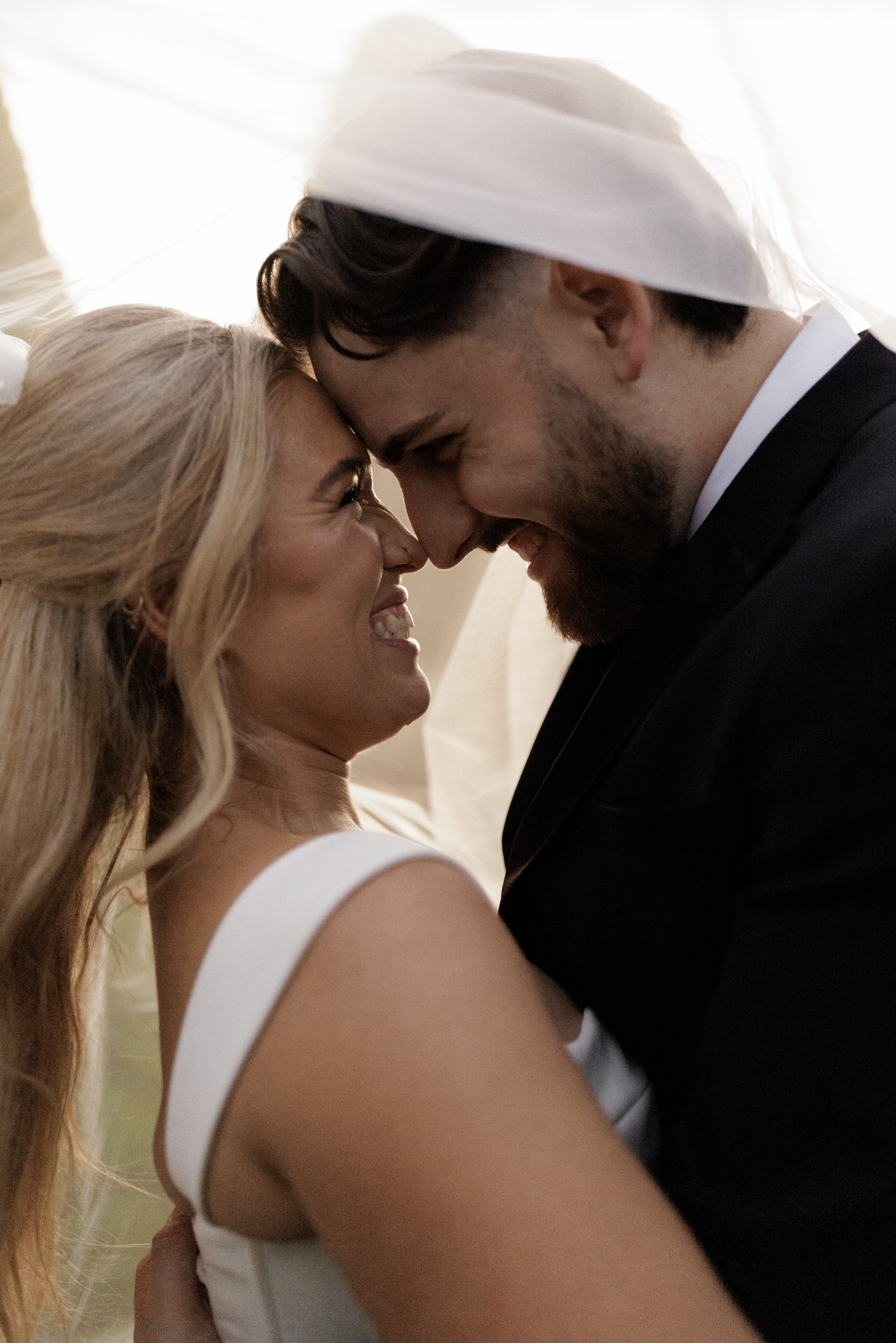 A couple with foreheads touching, smiling and gazing into each other's eyes, in a close, intimate moment.