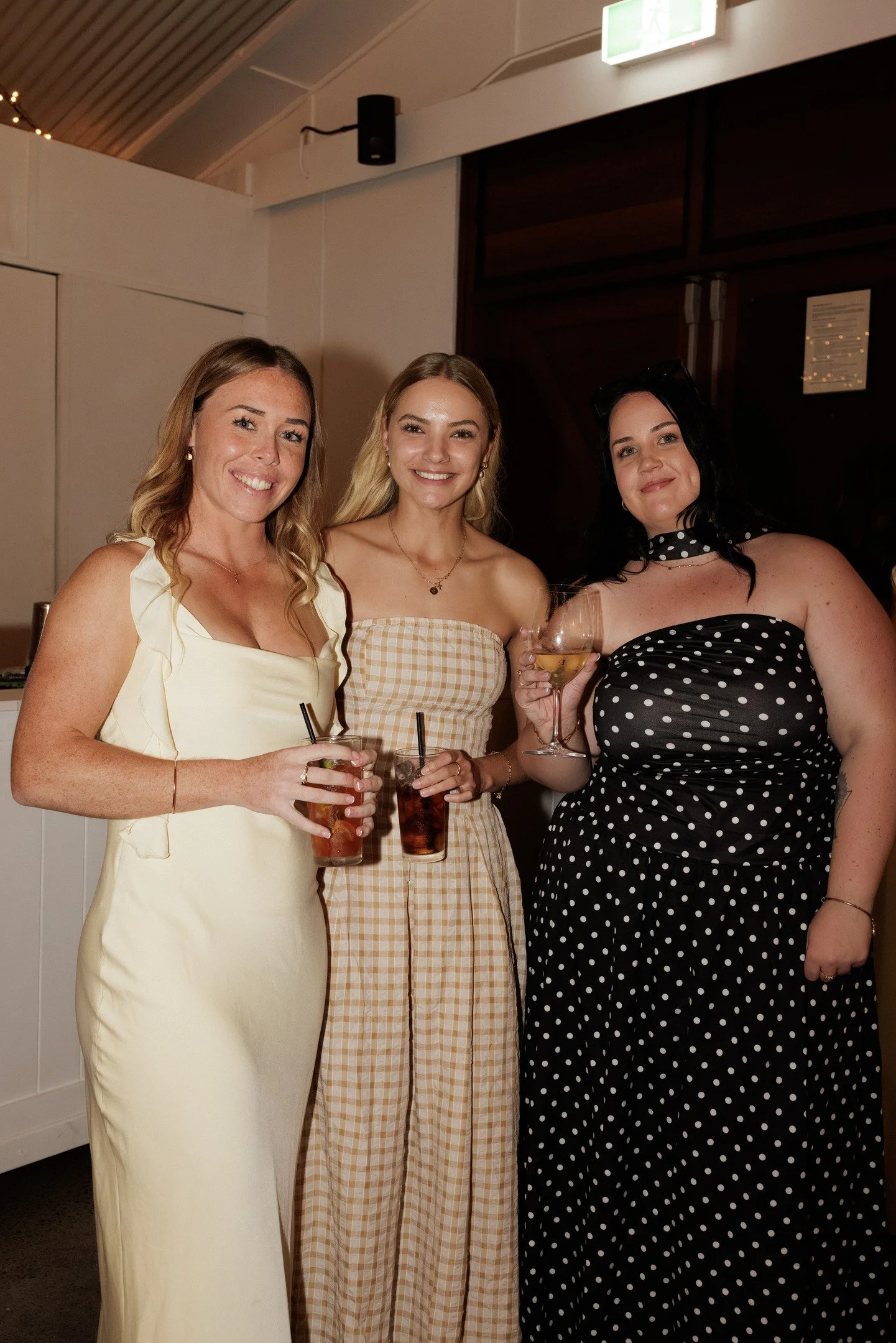 Three women standing together at a social event, smiling and holding drinks.