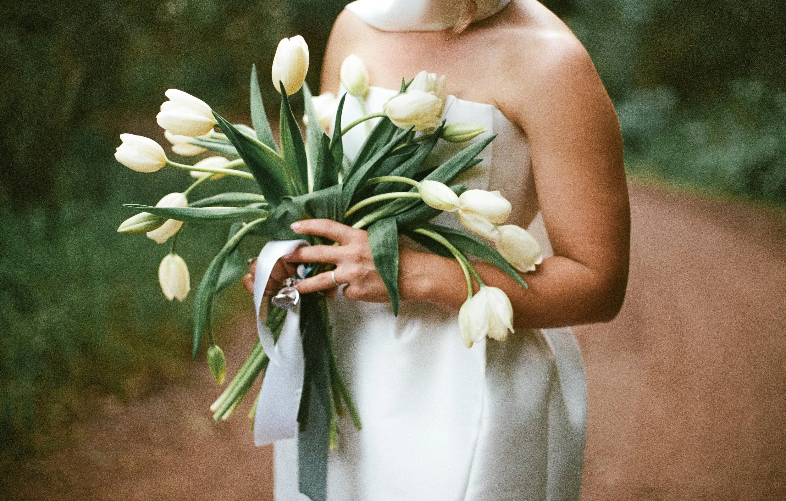 Bride holding a bouquet of white tulips on an outdoor path - shot on 35mm film for a nostalic feeling by Elevated Weddings