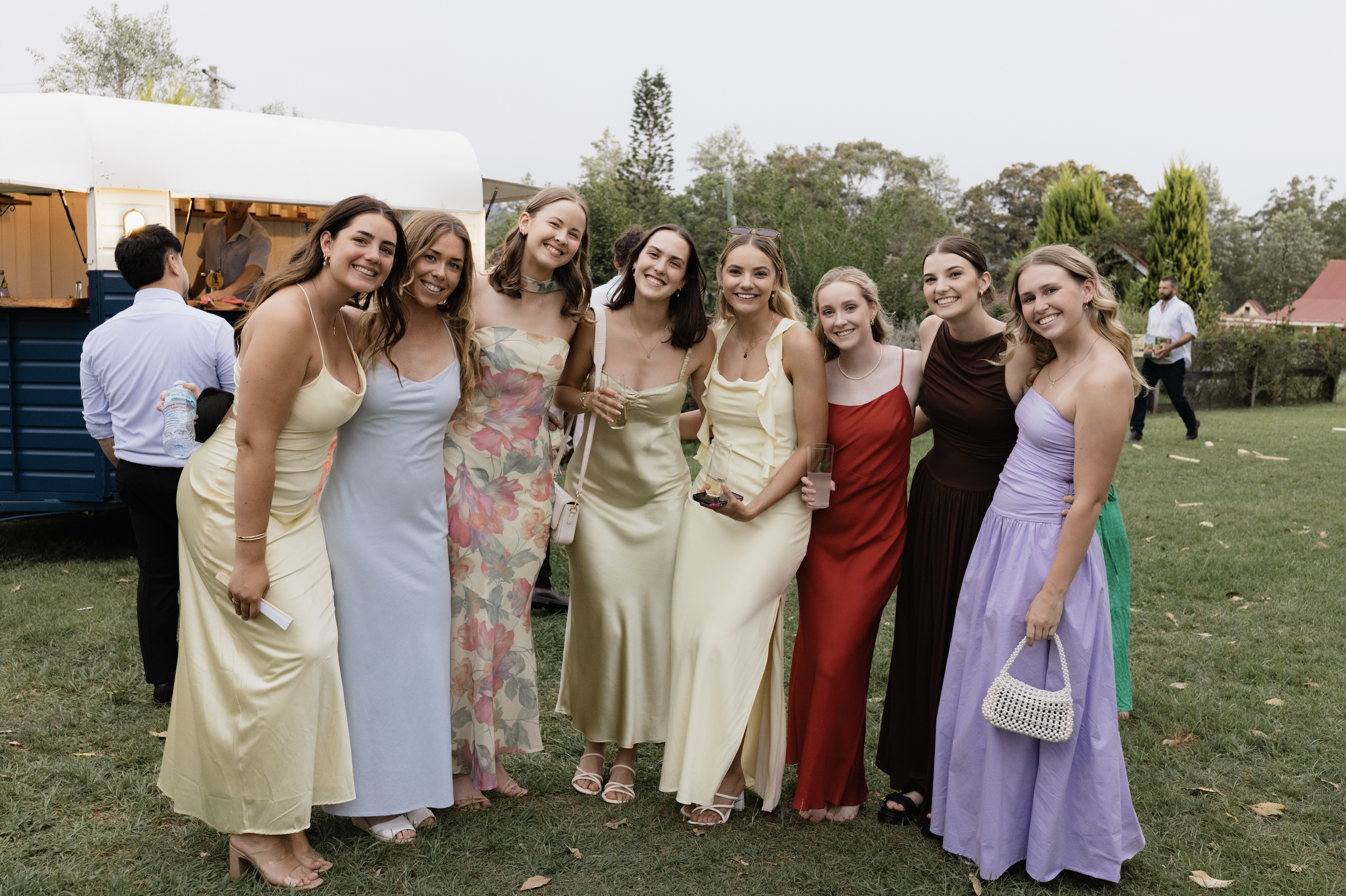 Group of women dressed in colorful dresses smiling outdoors at a gathering.