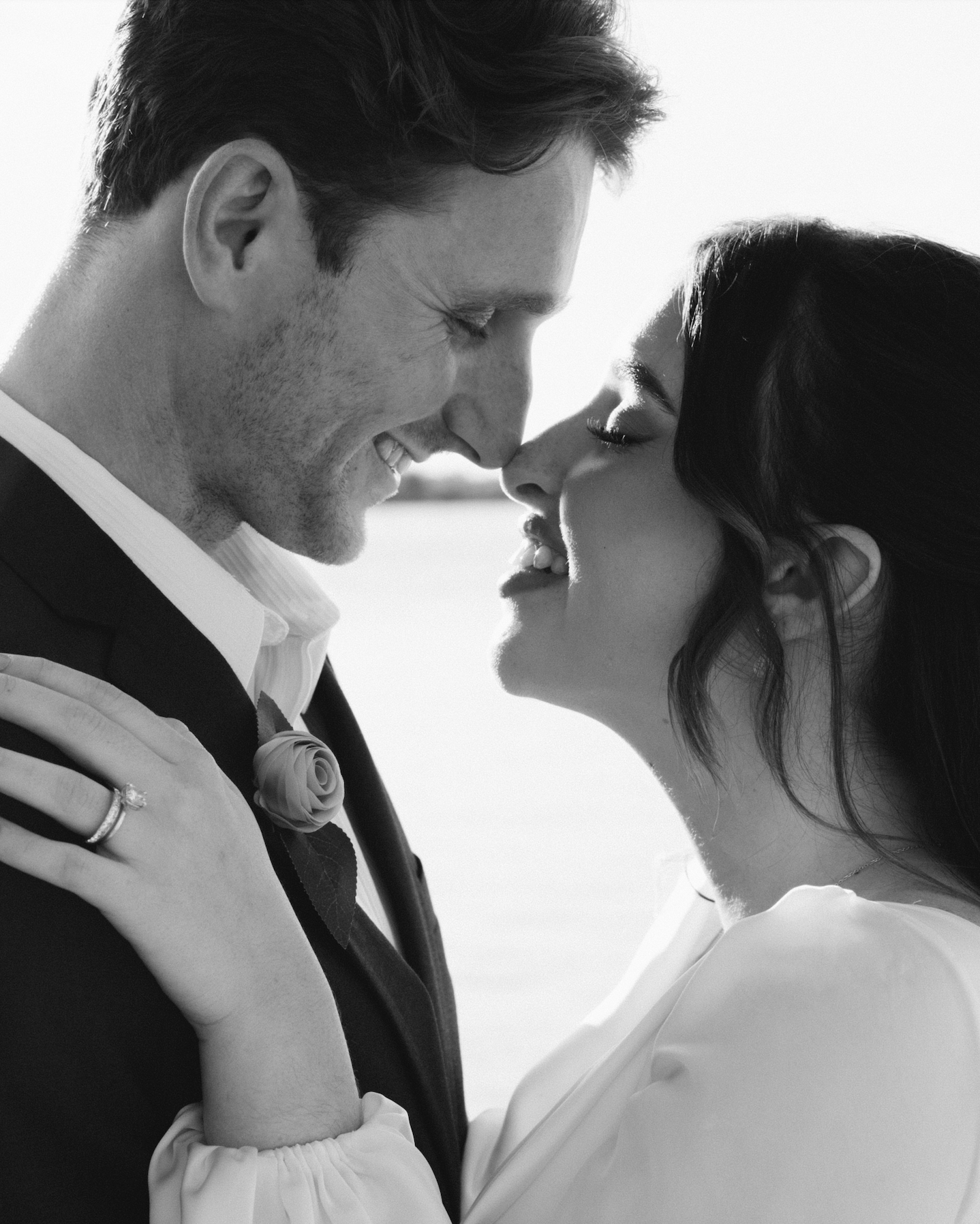 A black and white photo of a couple in a close embrace, smiling with their foreheads touching, outdoors.