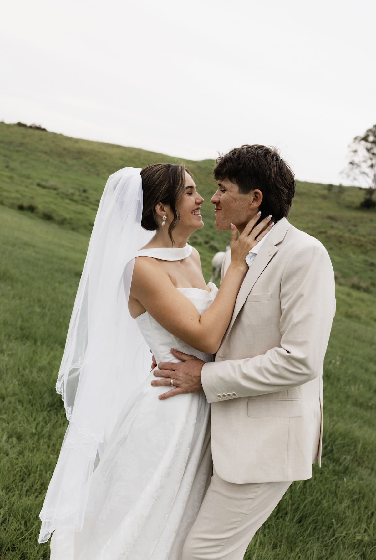 A bride and groom smiling closely in a green field, holding each other during a wedding photo.