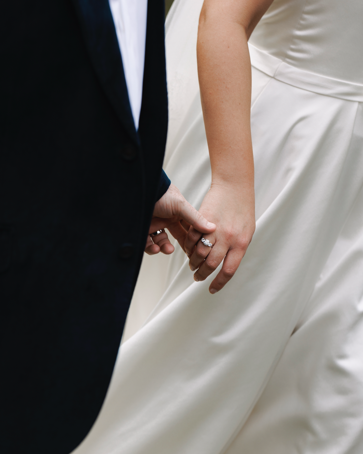 Close-up of a bride and groom holding hands during a wedding ceremony, focusing on the bride's engagement ring and wedding band.